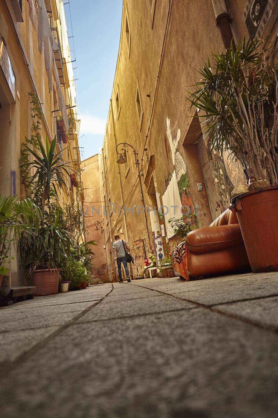 Shooting from the ground of a boy with shoulders walking along a colorful and characteristic alley of the city of Cagliari.
