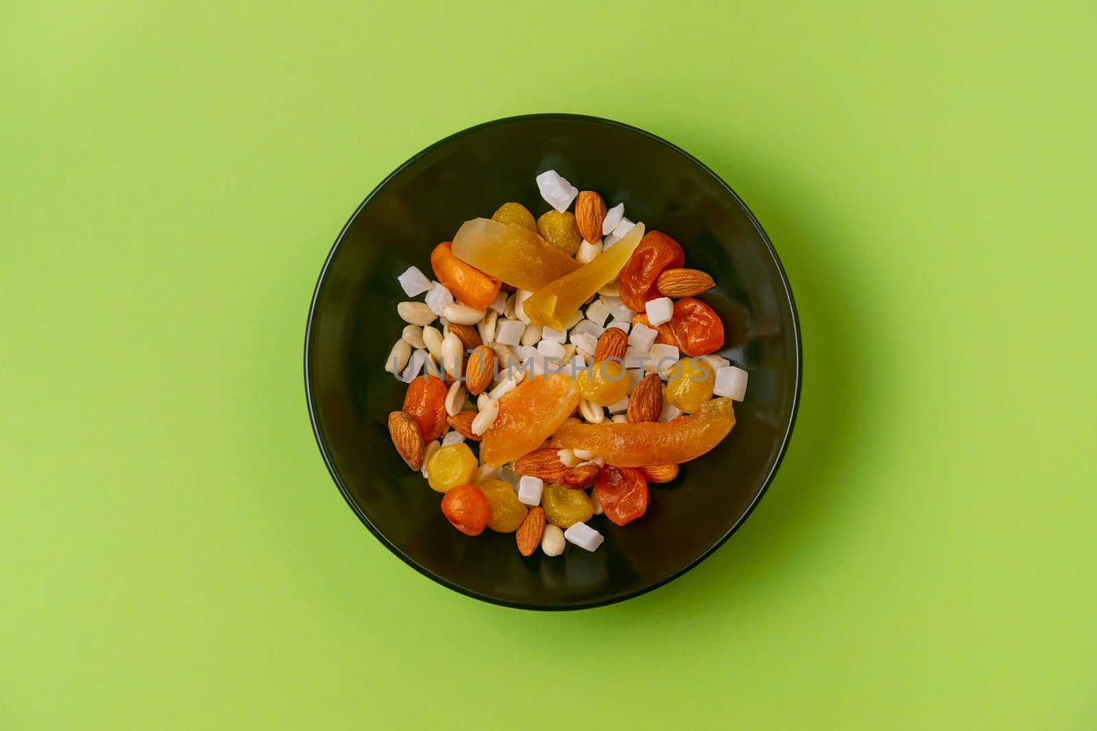 A fresh dried and candied fruits and nuts in black bowl on green by alexsdriver