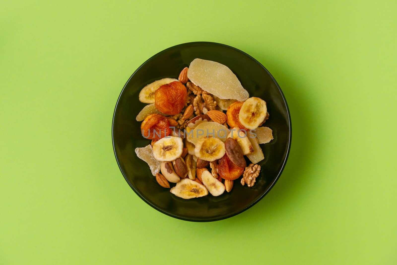 A fresh dried and candied fruits and nuts in black bowl on green bakground. Concept of nutrient and healty breakfast or meal and vegan or vegetarian food.