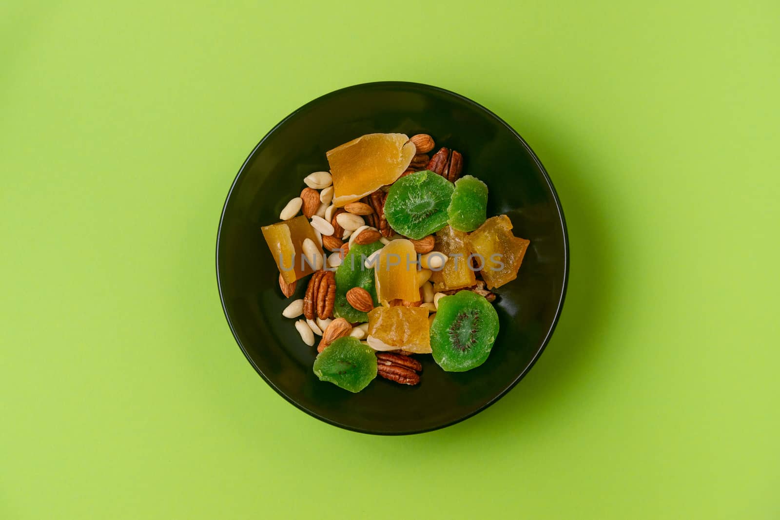 A fresh dried and candied fruits and nuts in black bowl on green bakground. Concept of nutrient and healty breakfast or meal and vegan or vegetarian food.