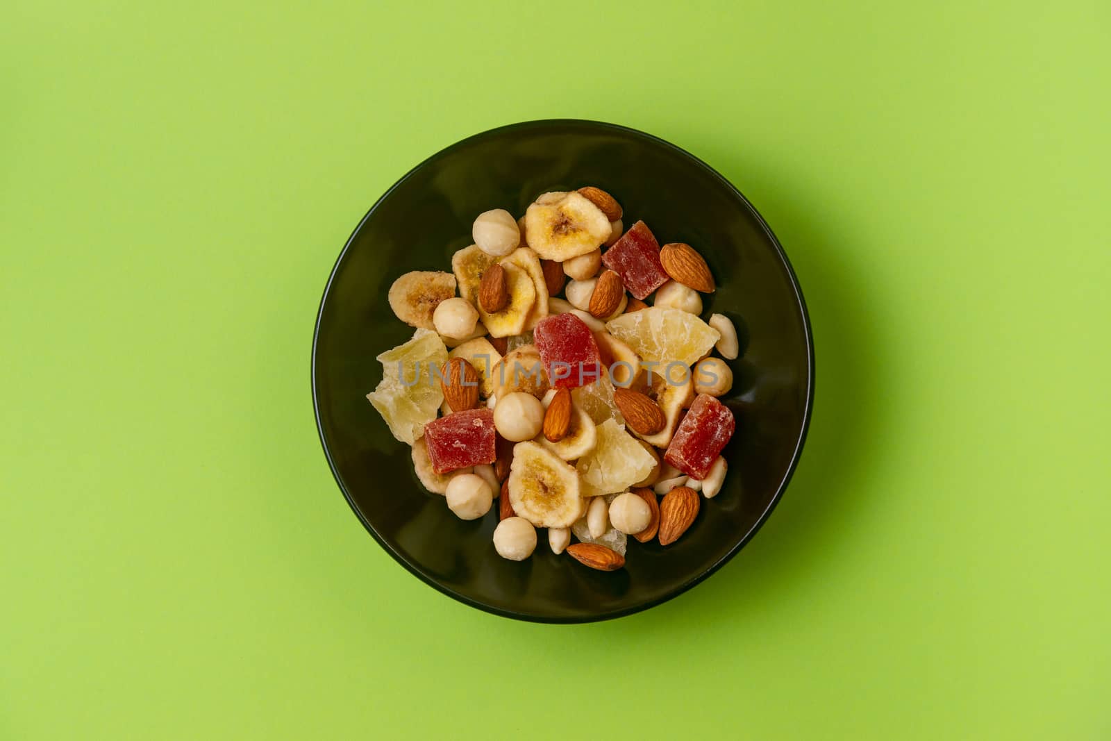 A fresh dried and candied fruits and nuts in black bowl on green bakground. Concept of nutrient and healty breakfast or meal and vegan or vegetarian food.