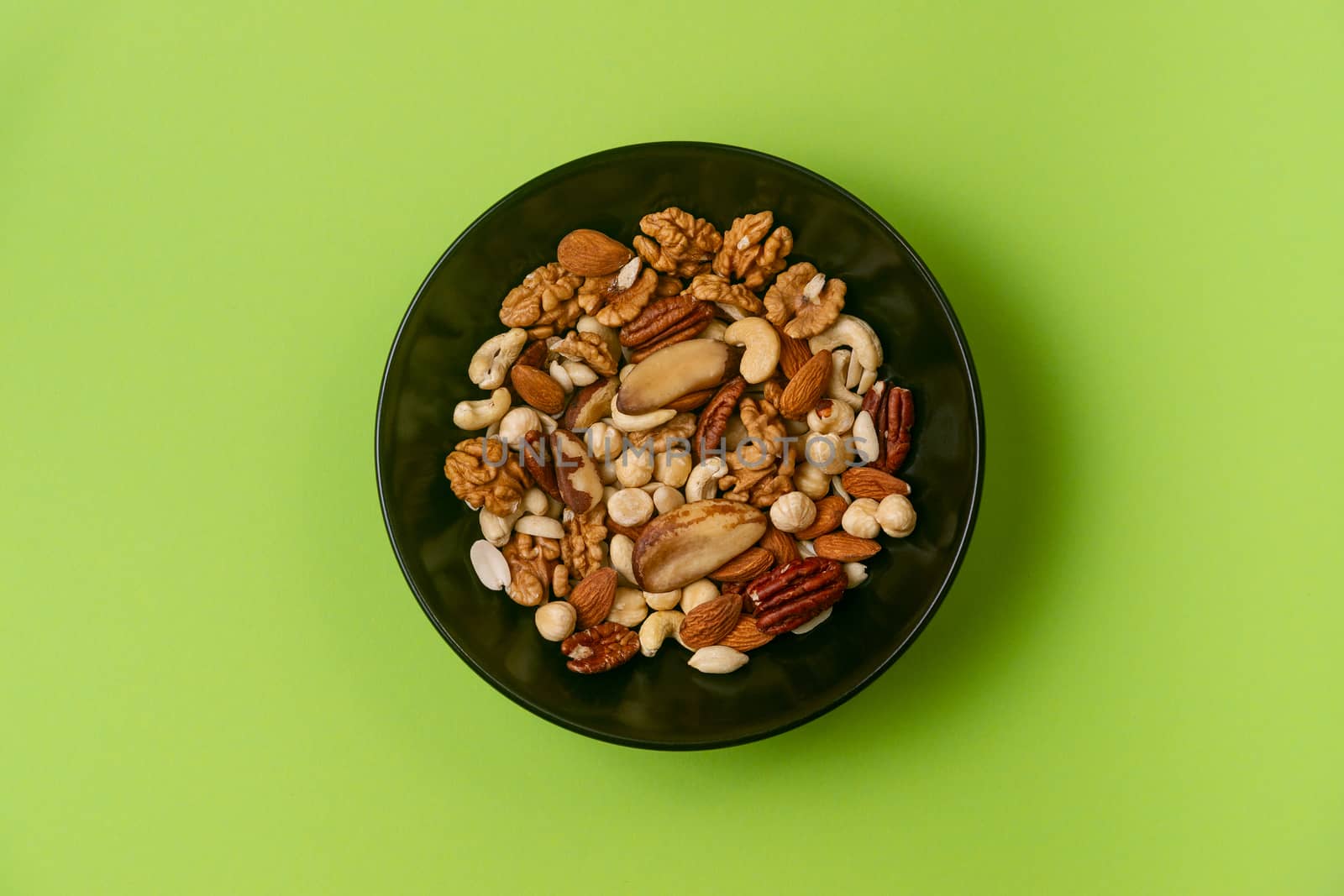 A fresh dried and candied fruits and nuts in black bowl on green bakground. Concept of nutrient and healty breakfast or meal and vegan or vegetarian food.