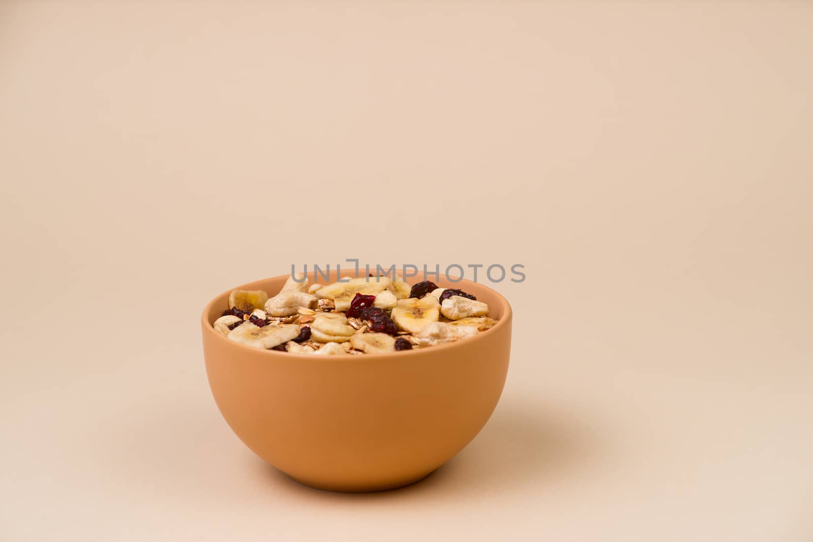 A fresh granola with dried and candied nuts and fruits in beige colour bowl closeup on beige bakground. Concept of nutrient and healty breakfast or meal