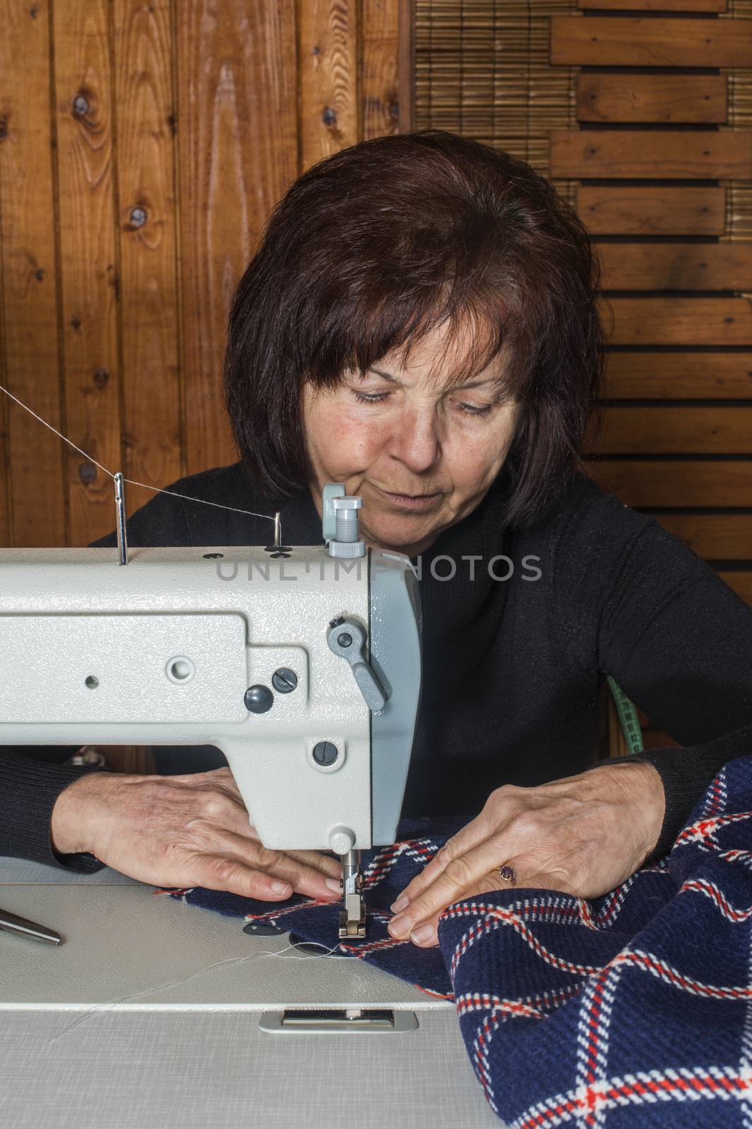 Woman sewing on a sewing machine. Wooden wall
