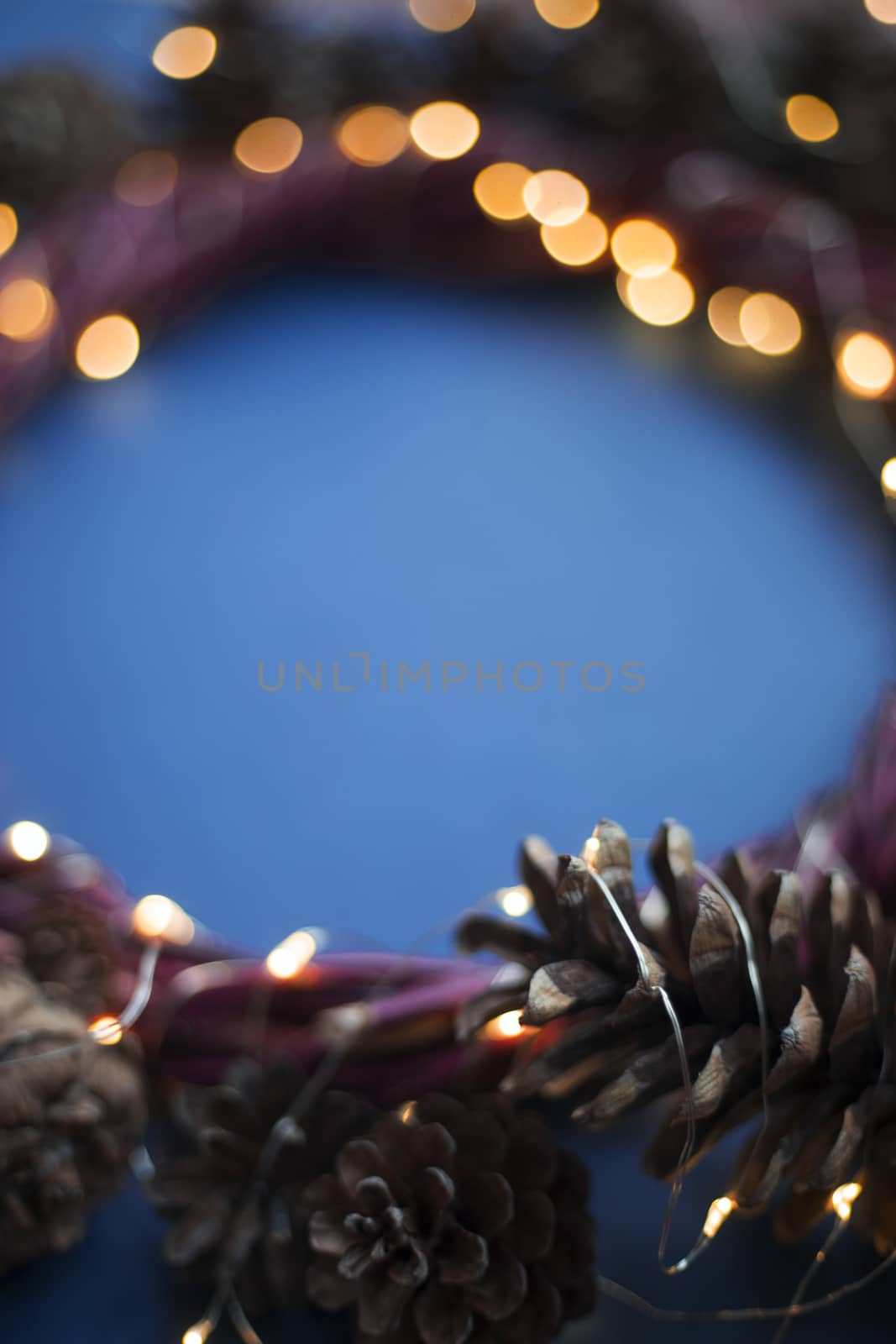Christmas wreath of pine cones and glowing lights garland on blue background copy space text