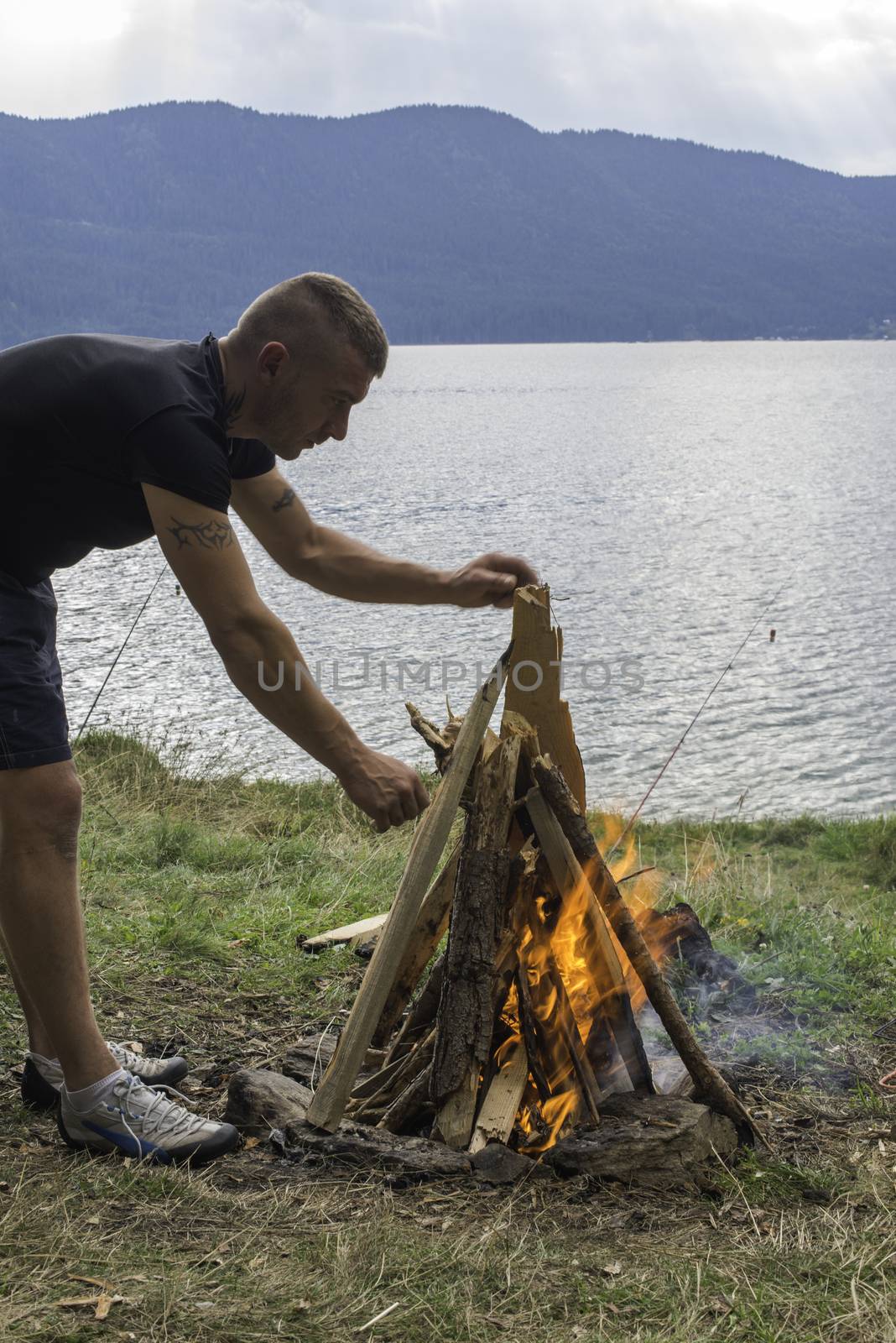 Boy who light fire in a forest. Lake on a background