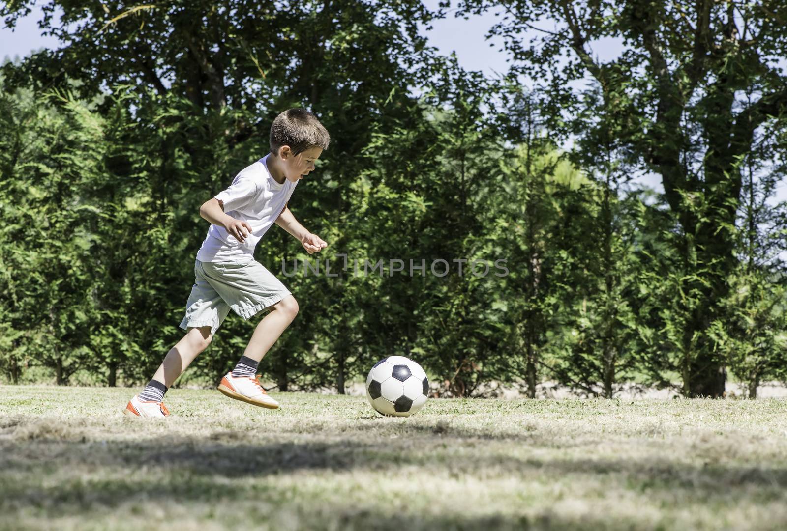 Child playing football in a stadium. Trees on the background