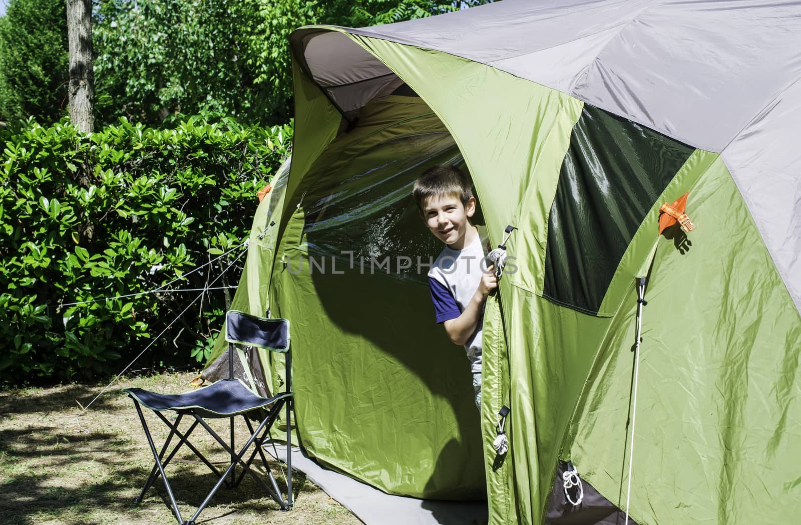 Child peeks from a green tent. Campsite