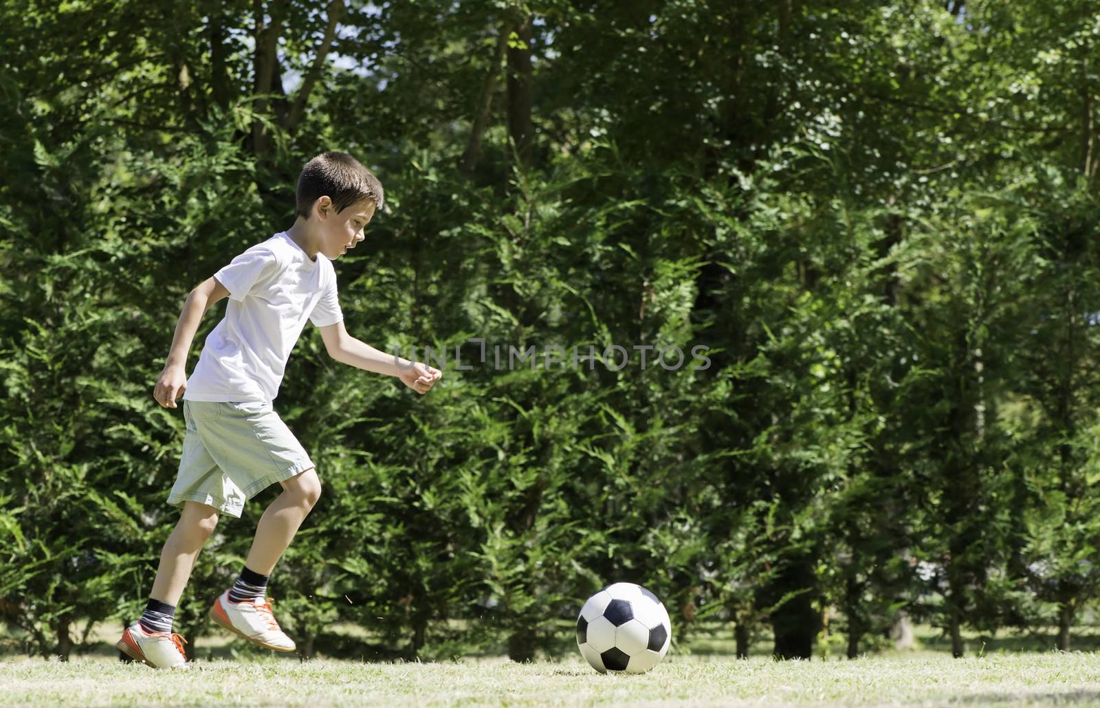 Child playing football in a stadium. Trees on the background
