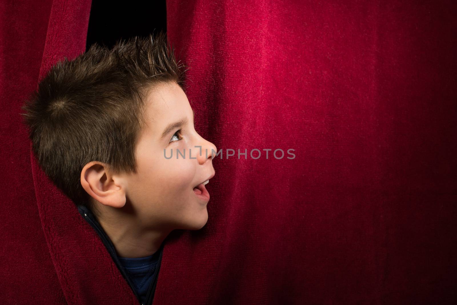 Child appearing beneath the curtain. Red curtain.