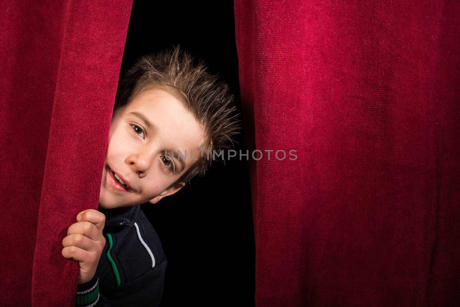 Child appearing beneath the curtain. Red curtain.