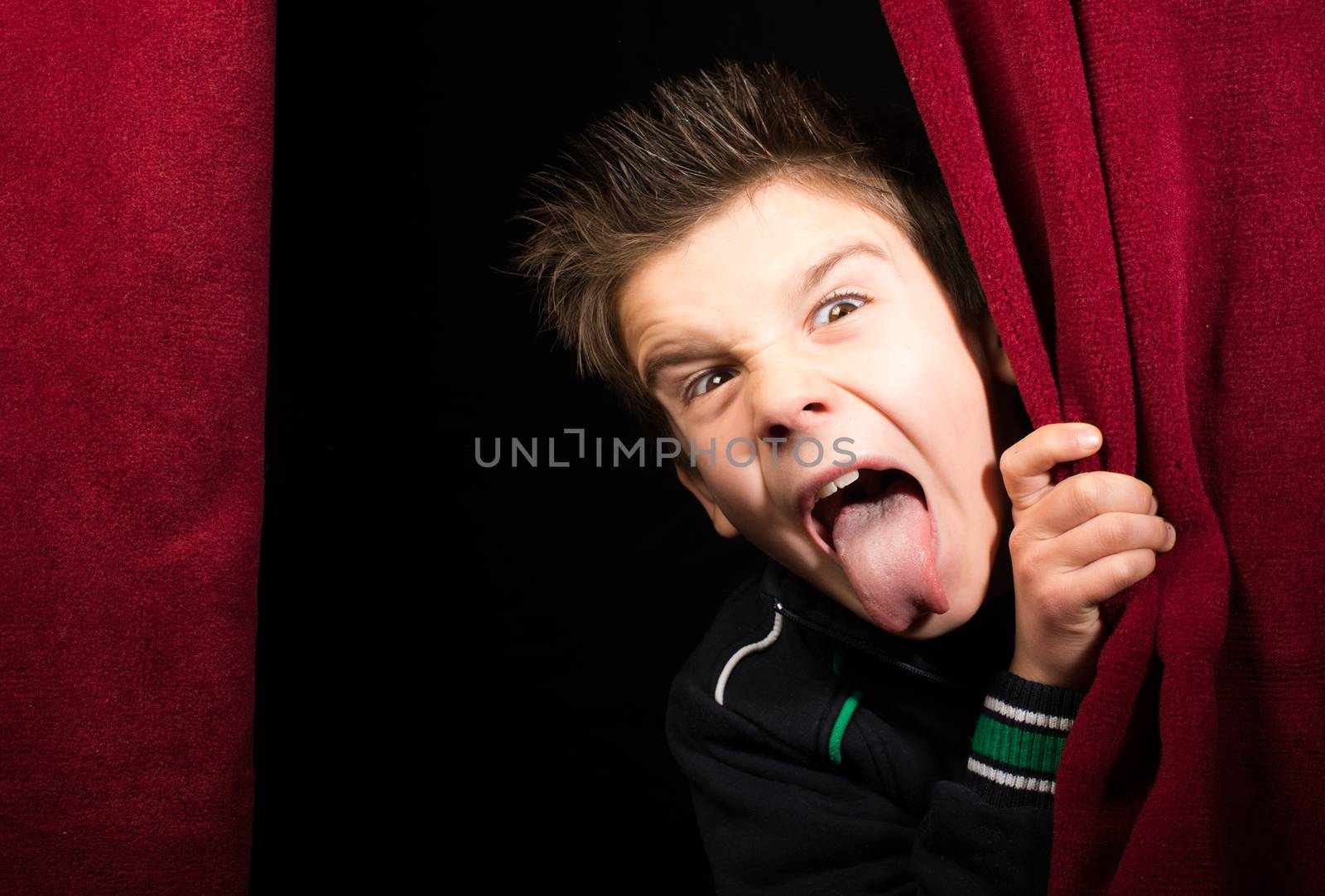 Child stick out his tongue.Appearing beneath the curtain