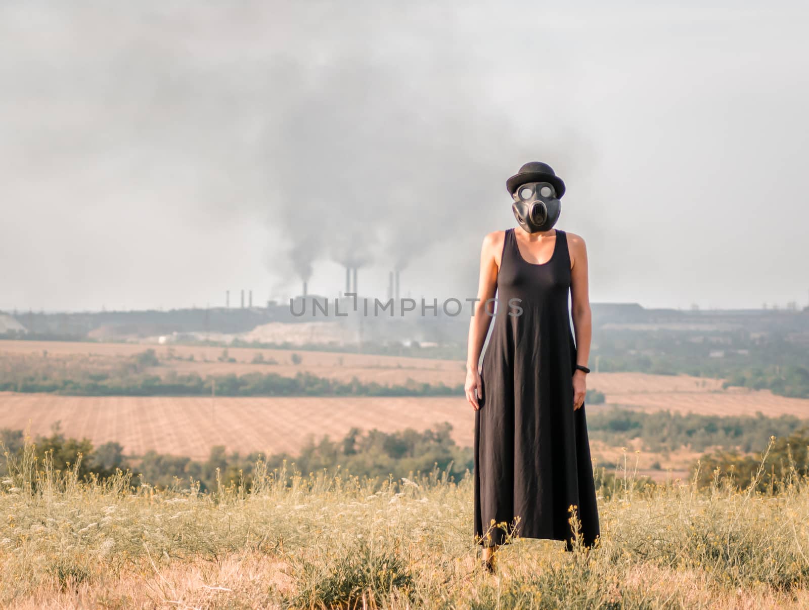young girl in a black dress and gas mask on the background of smoking factory chimneys
