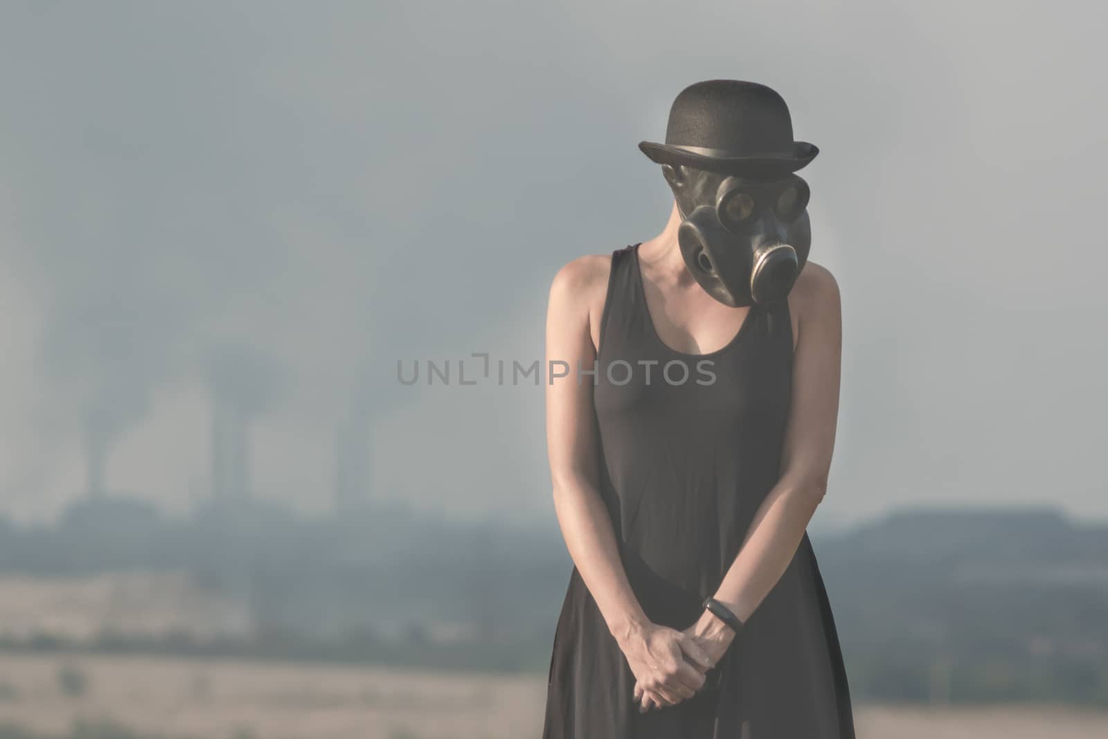 young girl in a black dress and gas mask on the background of smoking factory chimneys close up