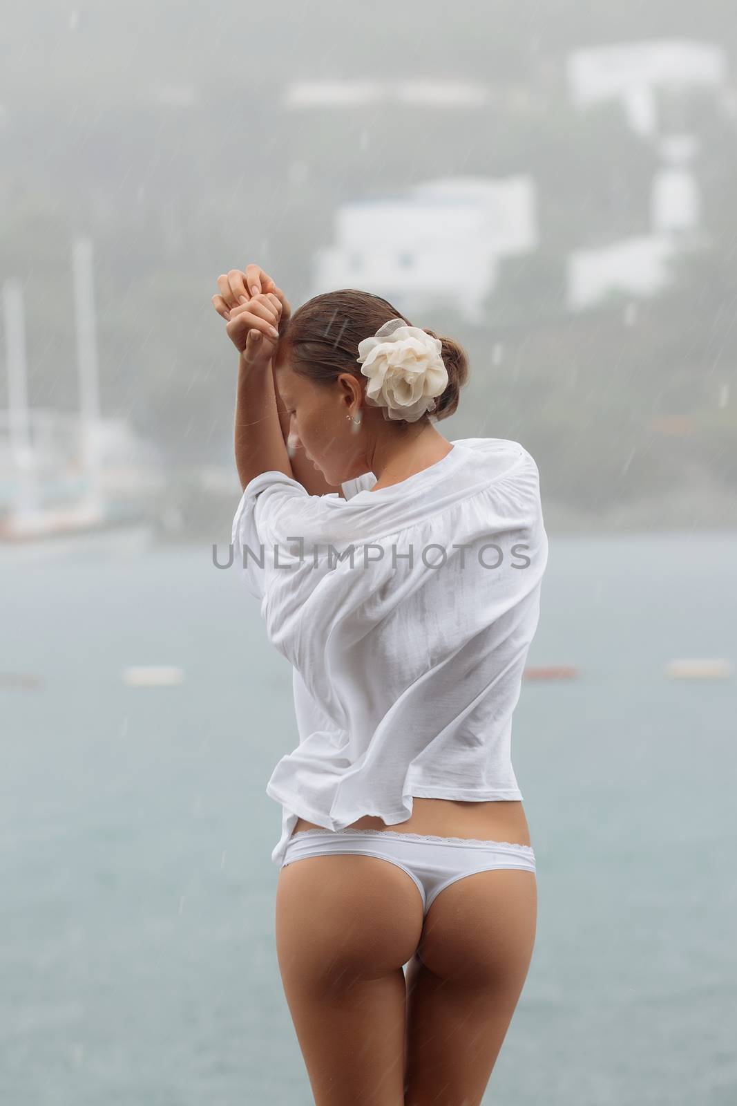 Back view of sensual female in white blouse and panties standing near sea on windy and rainy day