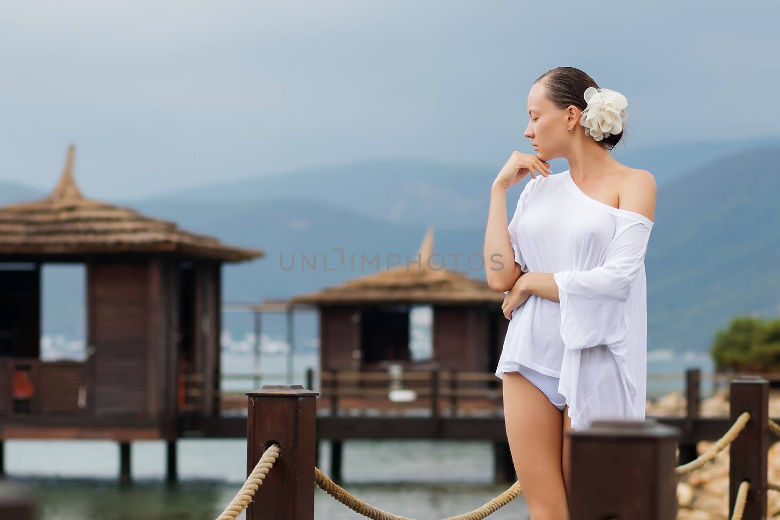 Lovely young female in stylish white blouse keeping eyes closed while standing on background of wonderful resort