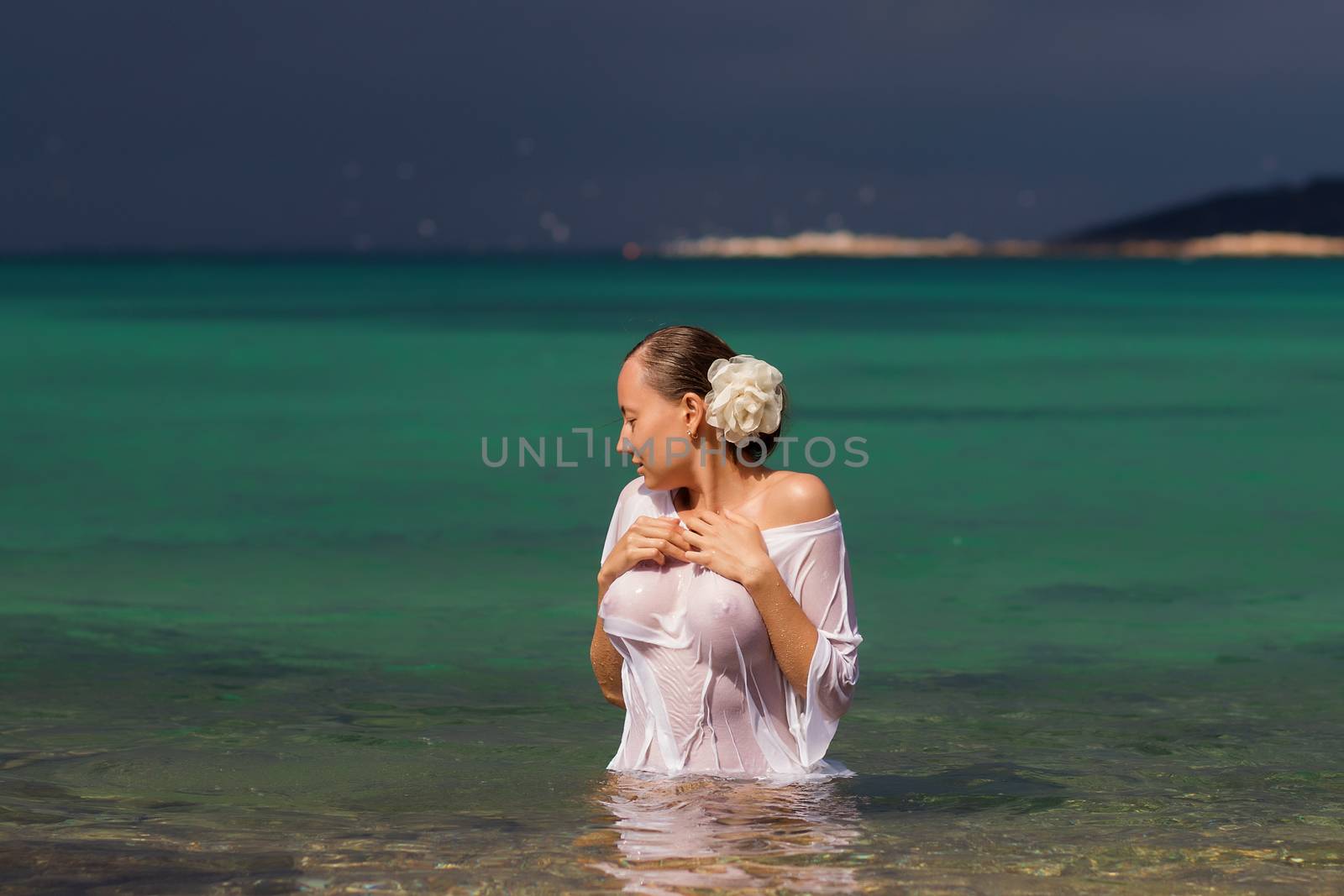 Sensual young female in wet blouse standing in clean sea water and looking away