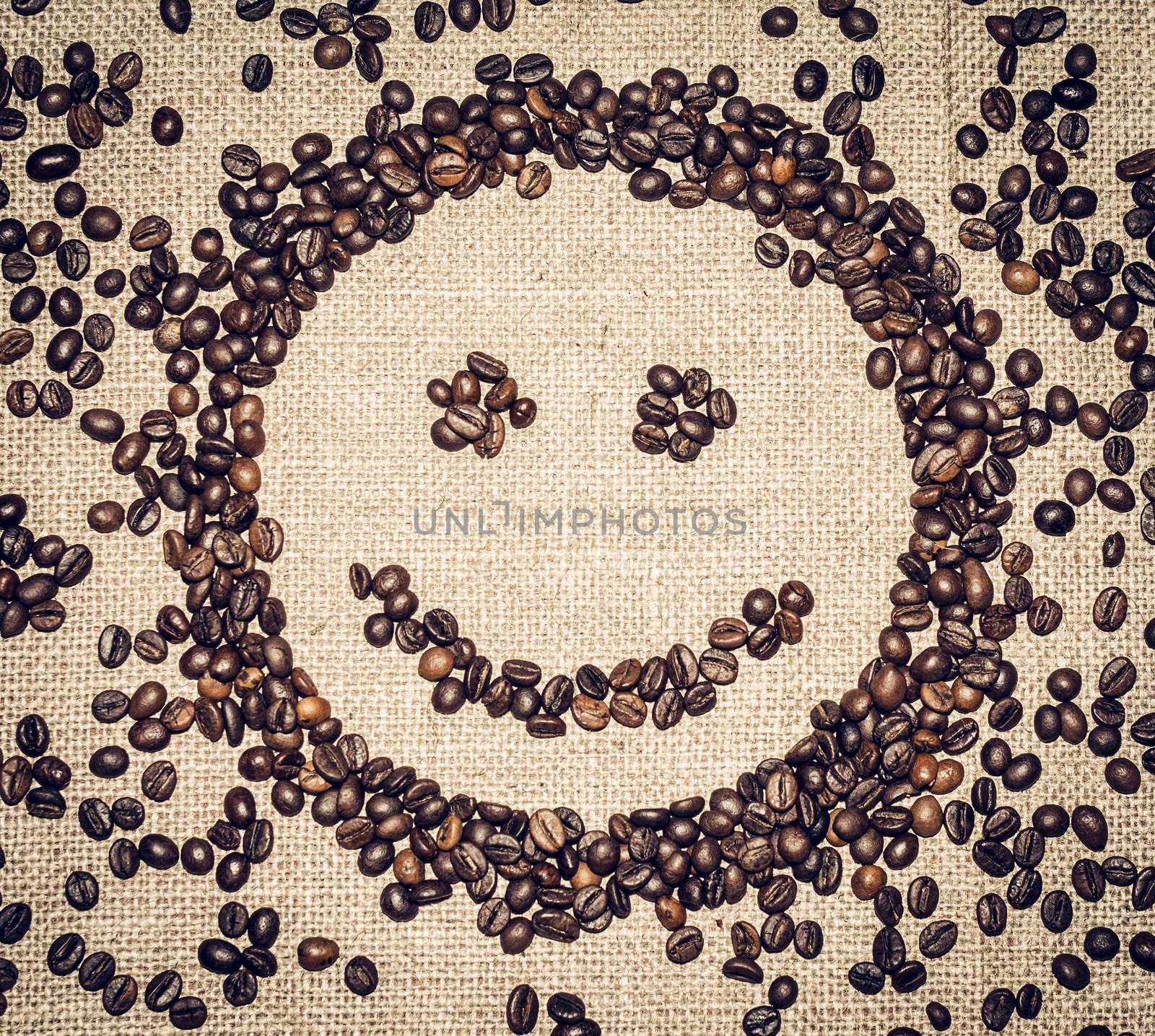 smiling face formed by coffee grains on a coarse cloth surrounded by coffee beans
