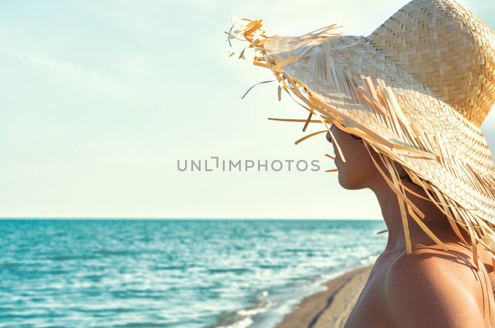 young girl in a straw hat on the background of the surf of the sea and sky with clouds close up