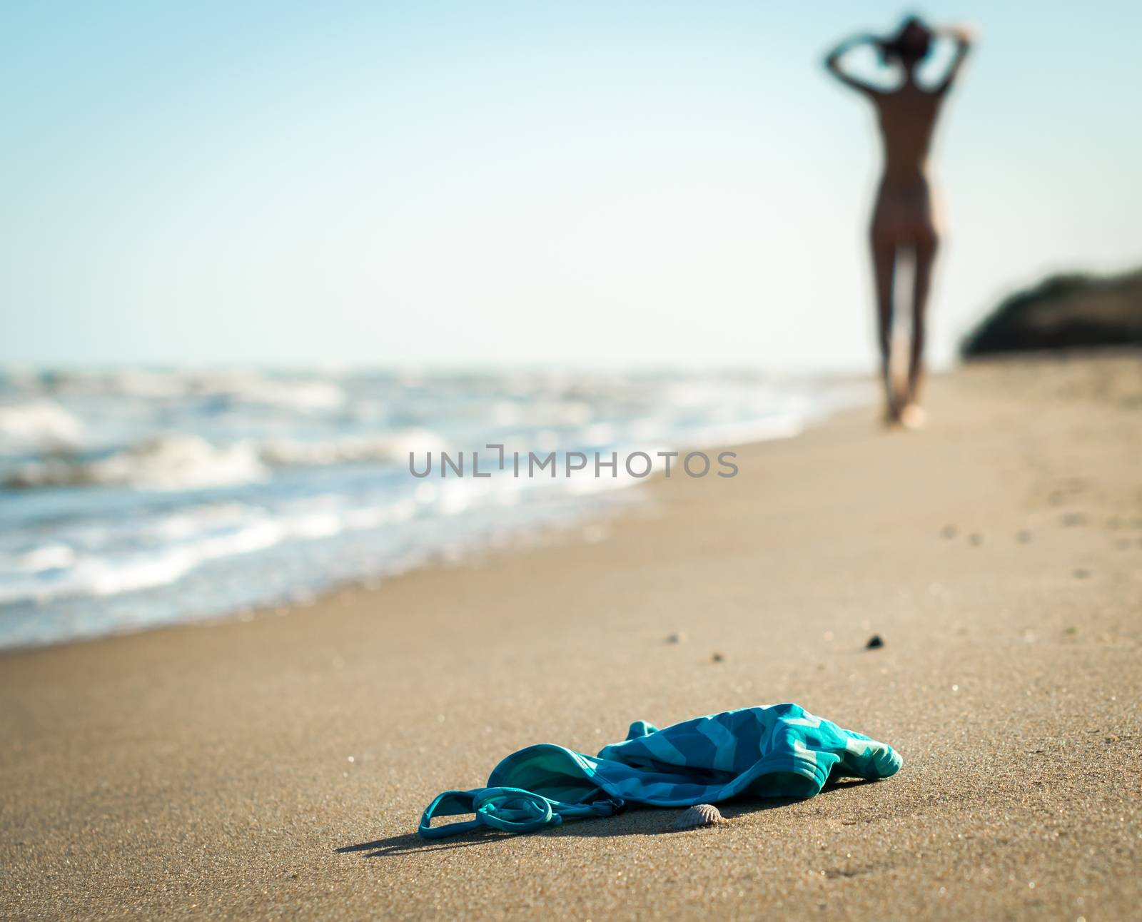 swimsuit in the sand on the beach near the sea surf on the background of a naked female figure and blue sky