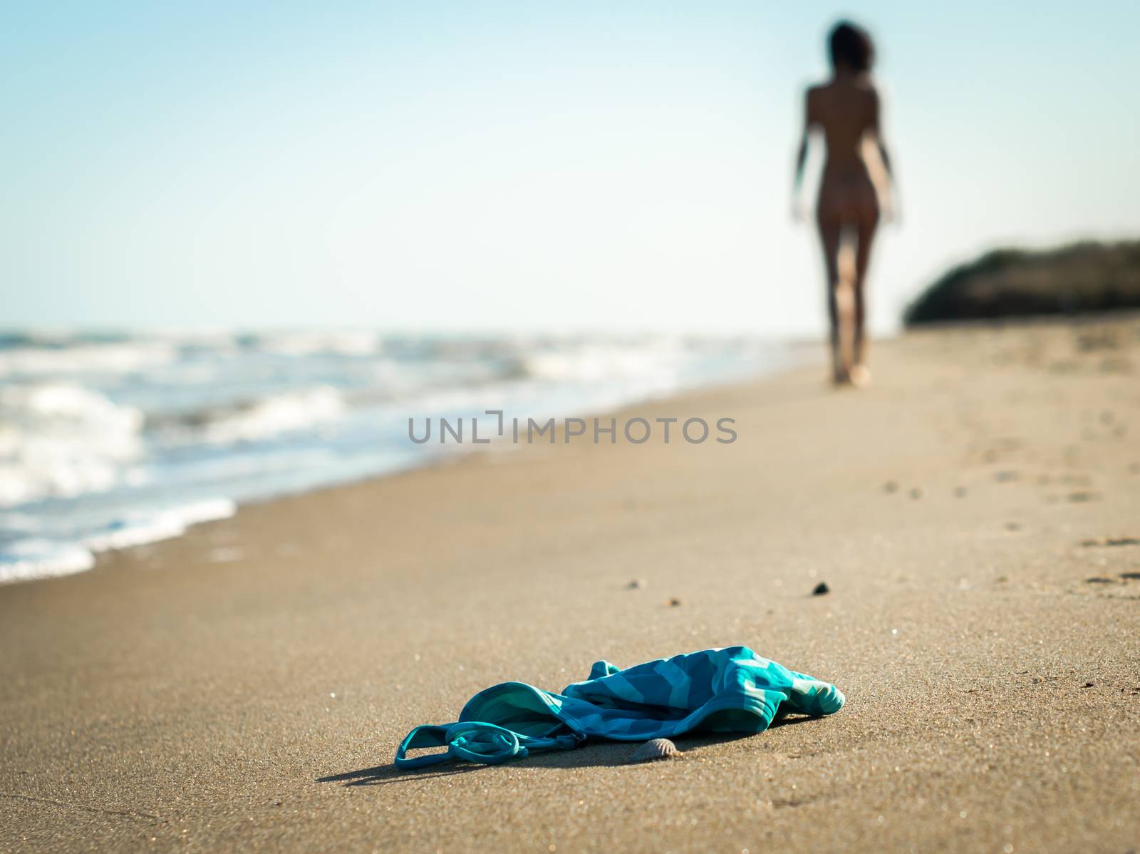swimsuit in the sand on the beach near the sea surf on the background of a naked female figure and blue sky