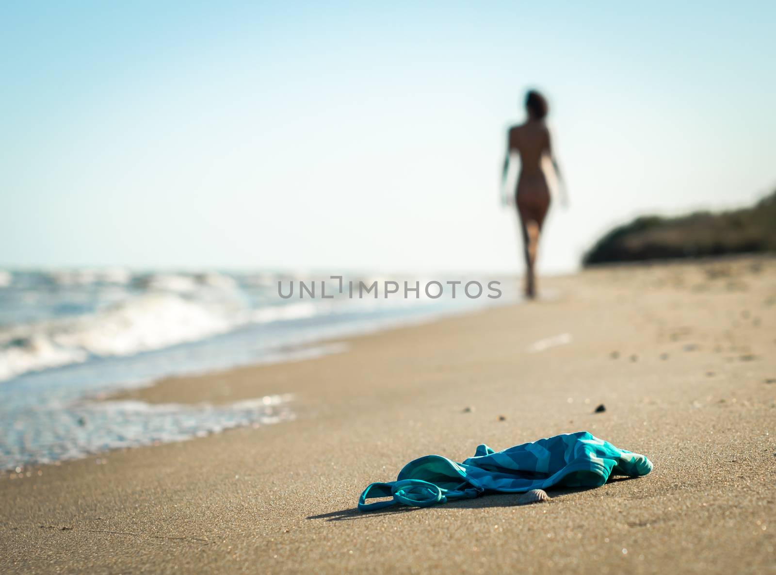 swimsuit in the sand on the beach near the sea surf on the background of a naked female figure and blue sky