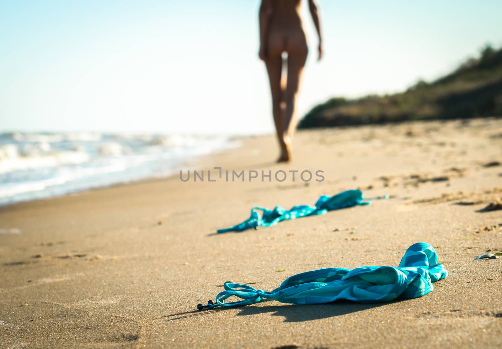 swimsuit in the sand on the beach near the sea surf on the background of a naked female figure and blue sky