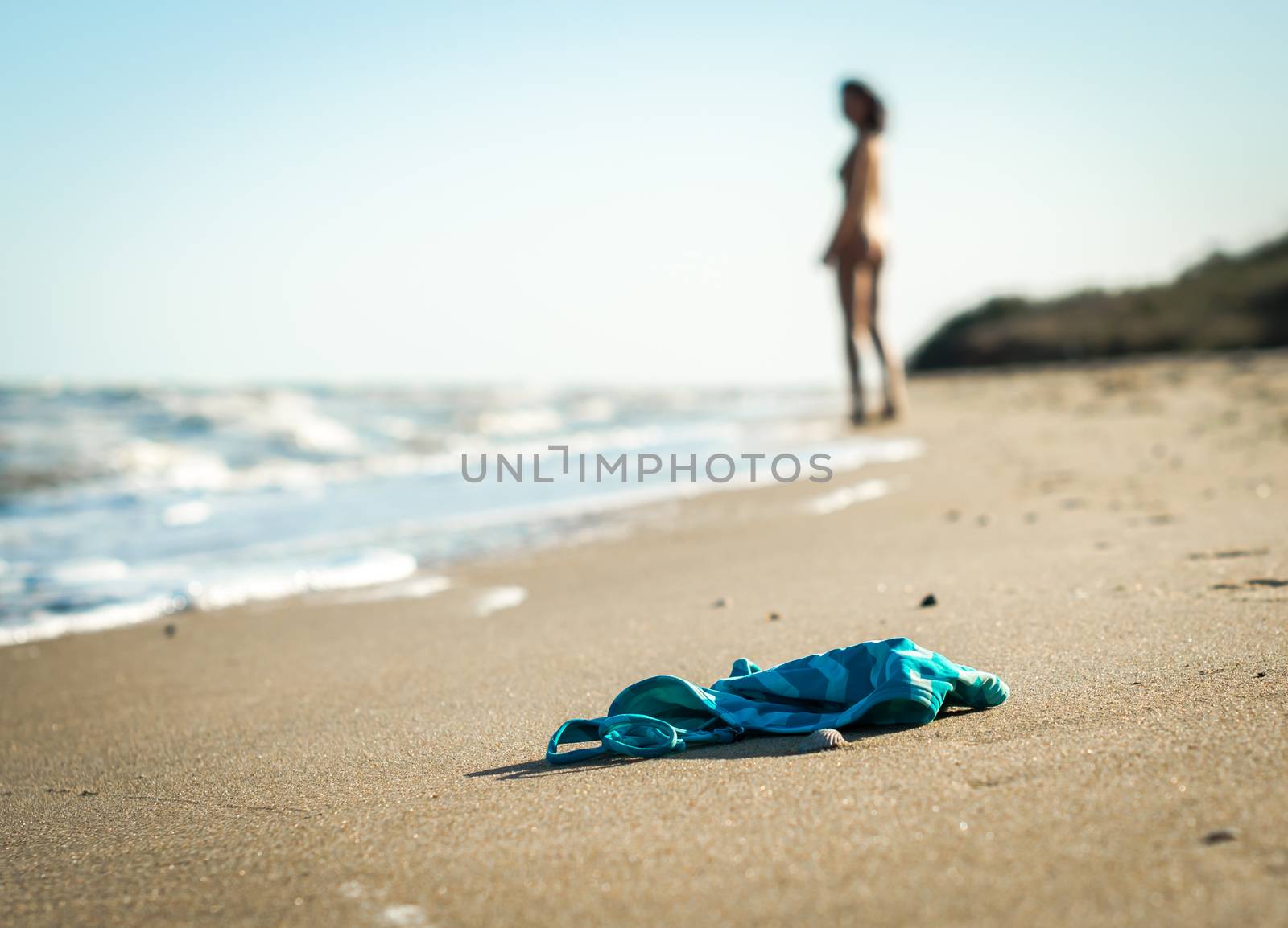 swimsuit in the sand on the beach near the sea surf on the background of a naked female figure and blue sky