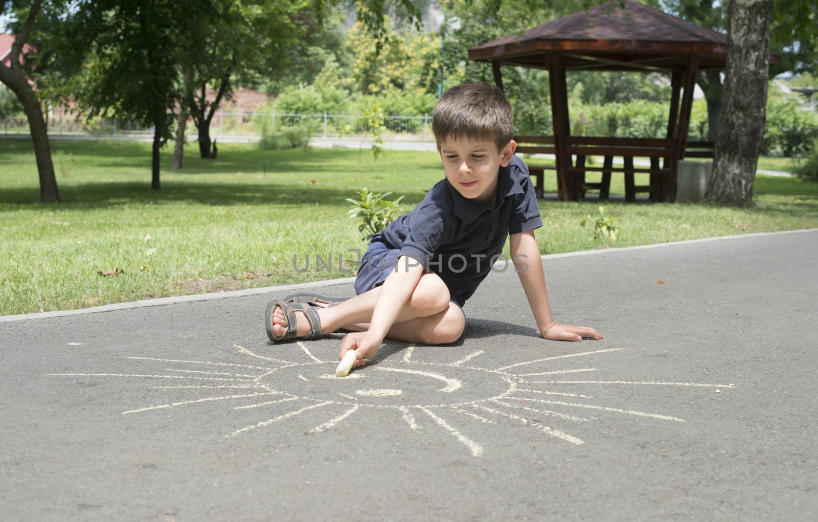 Child drawing sun on asphalt in a park