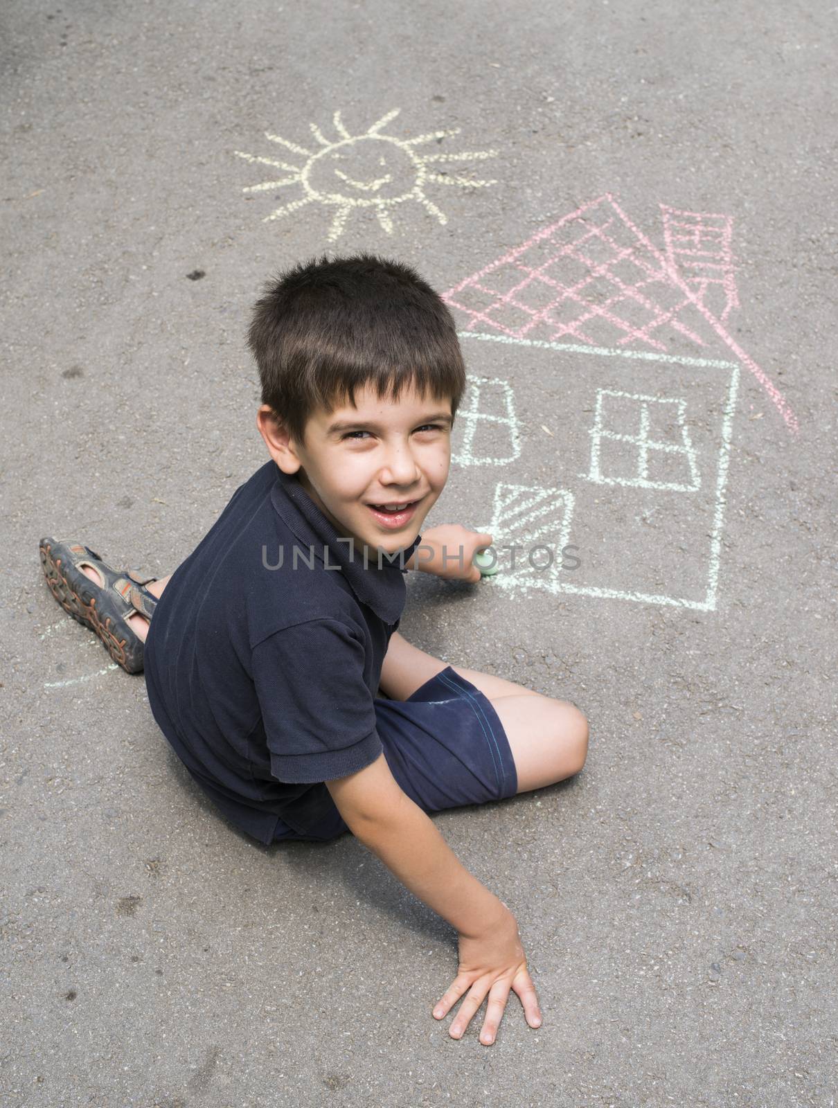 Child drawing sun and house on asphalt in a park