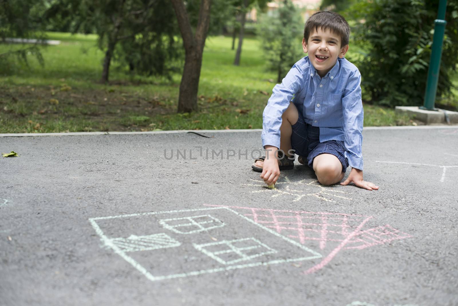 Child drawing sun and house on asphalt in a park