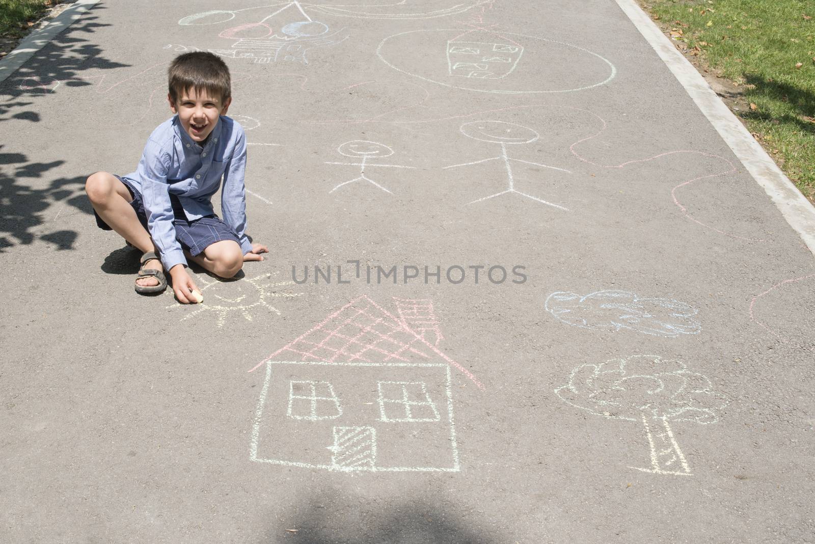 Child drawing sun and house on asphalt in a park