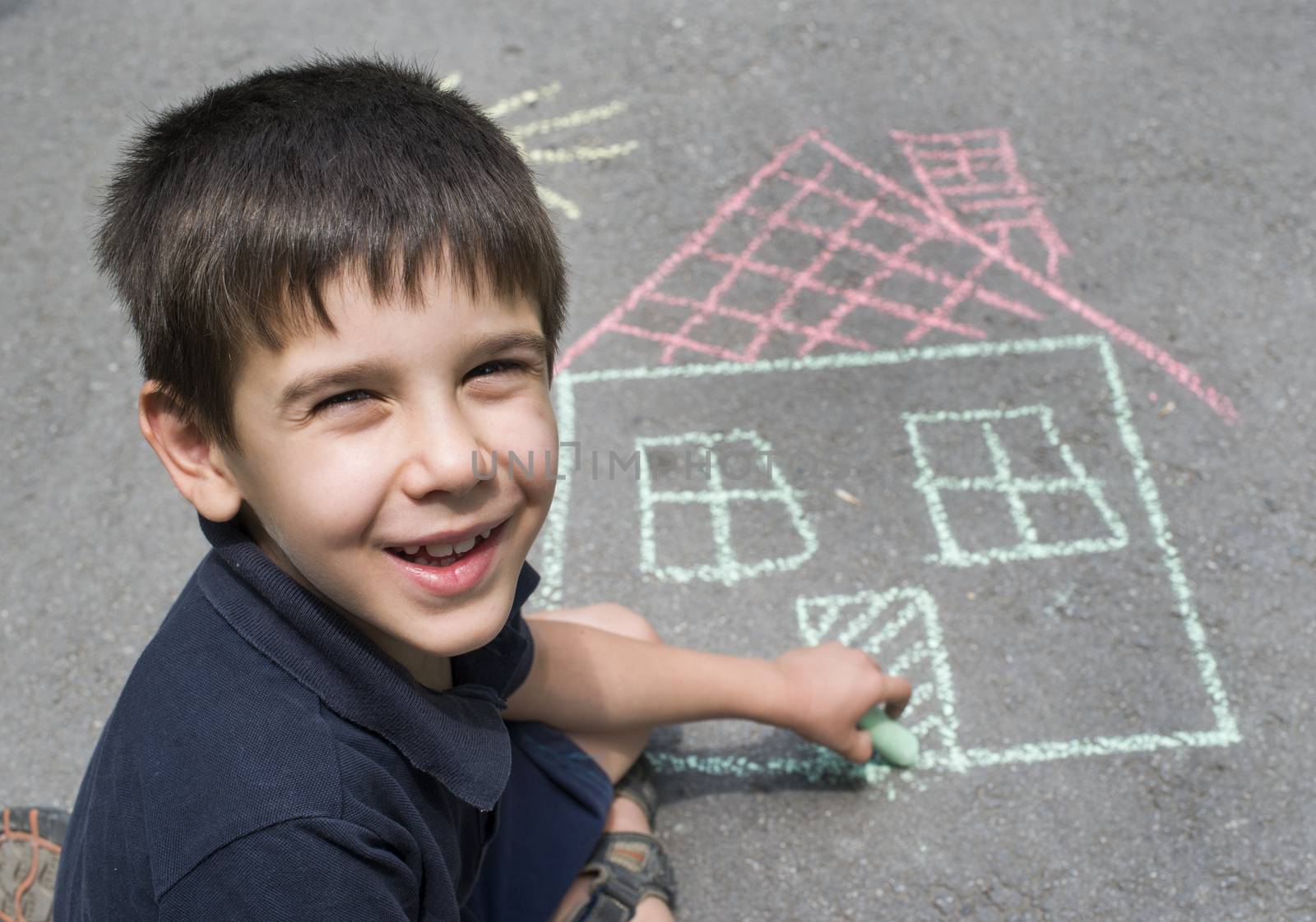 Child drawing sun and house on asphalt in a park
