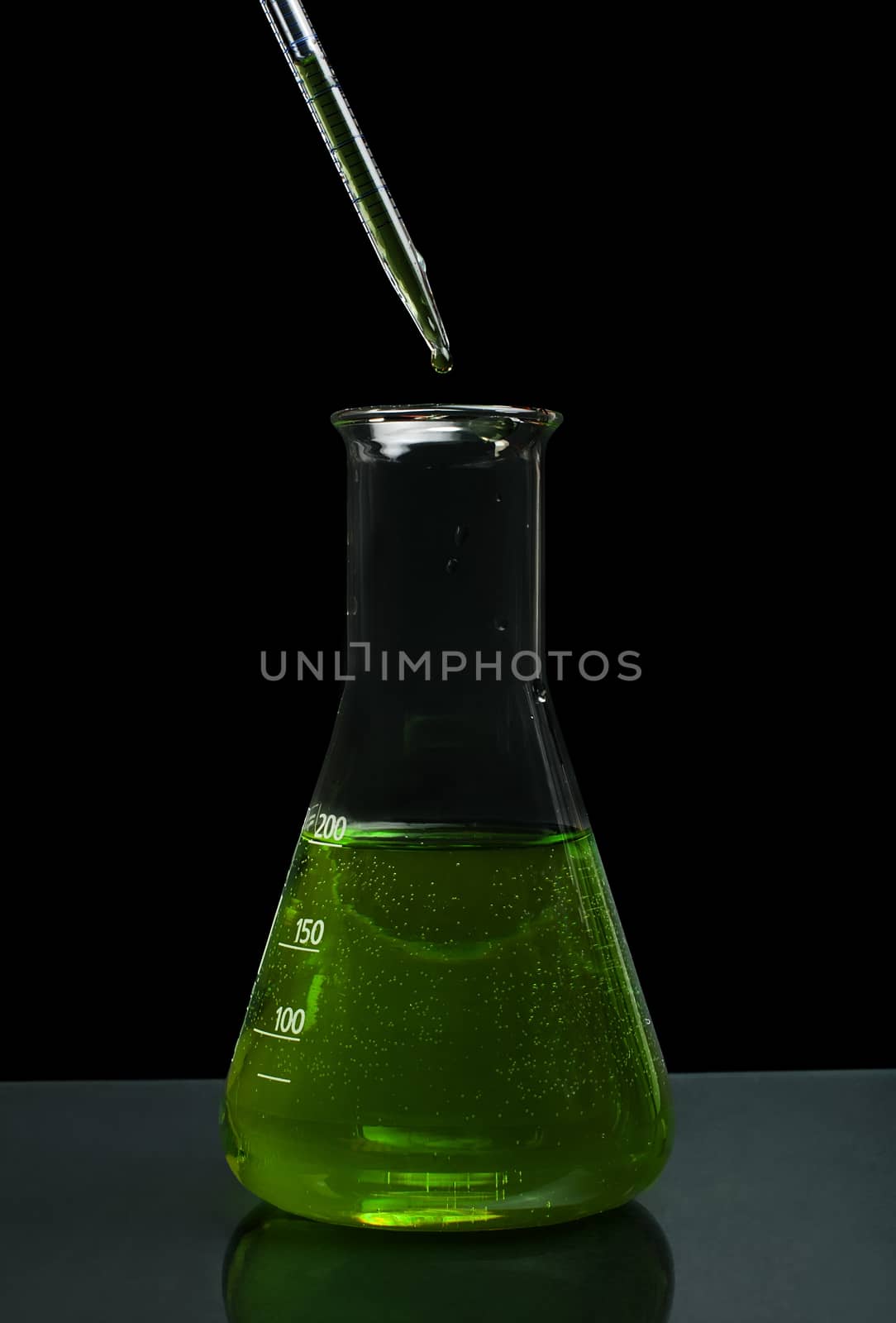 Laboratory beaker filled with green color liquid substances and laboratory pipette. Dark background
