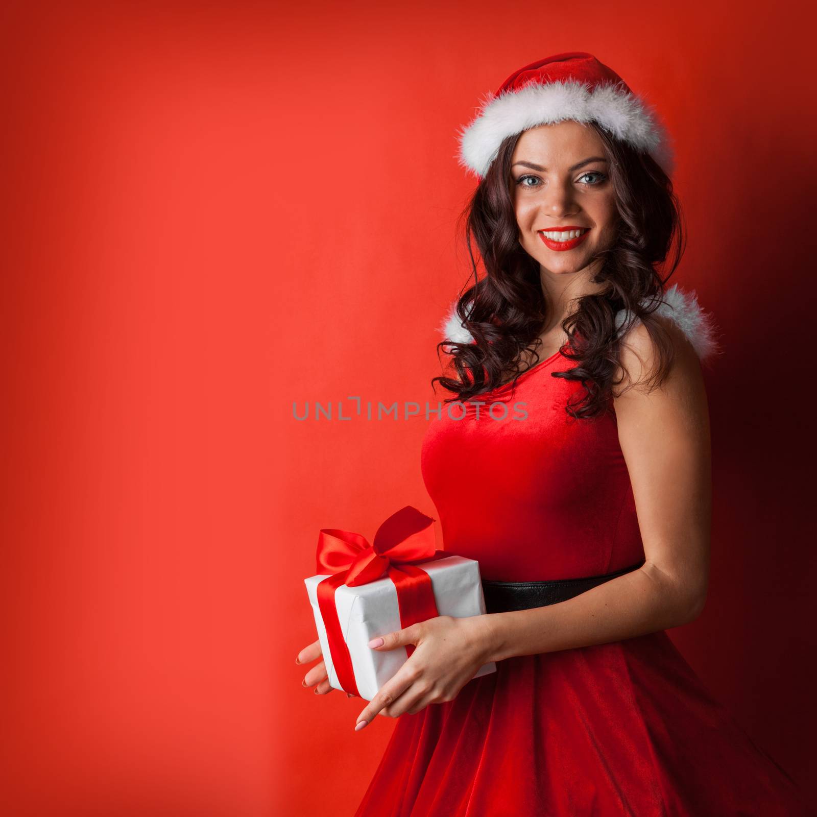 Beautiful young woman in Santa dress and hat celebrating Christmas holding gift box