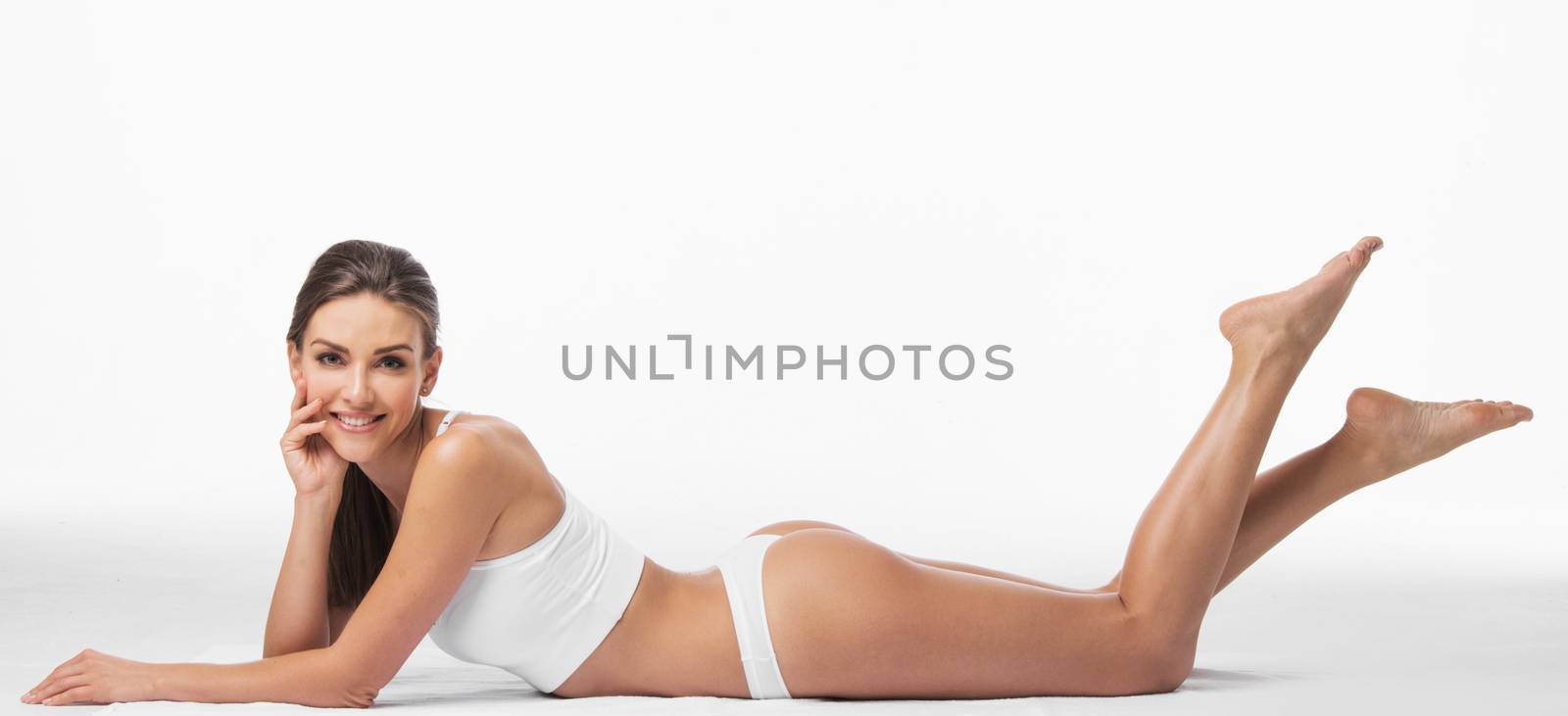 Attractive young woman in underwear is laying and smiling with happiness. Isolated on background