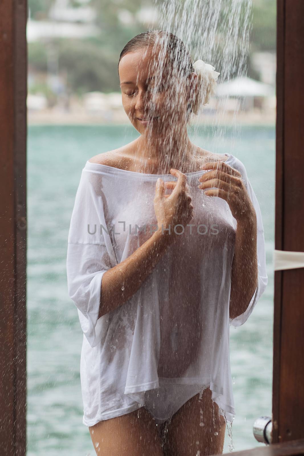 Crop young lady in wet white blouse embracing herself trying to avoid splash of clean water