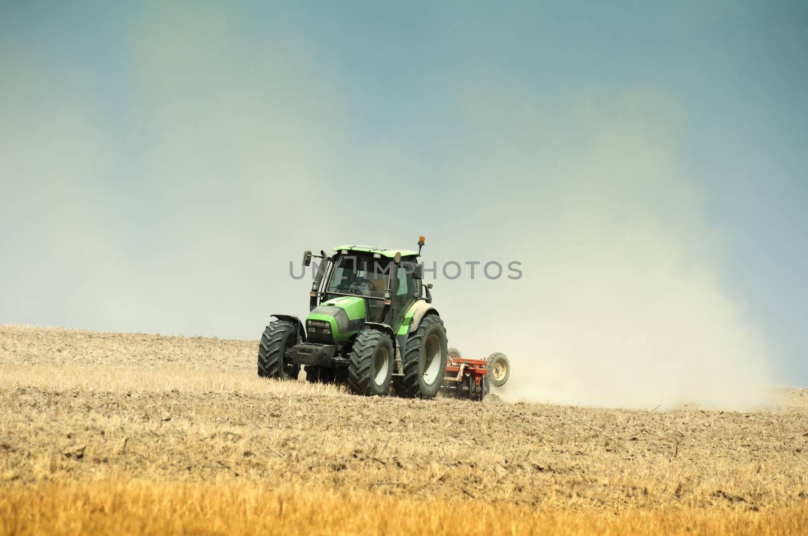 Tractor plowing field on blue sky background.