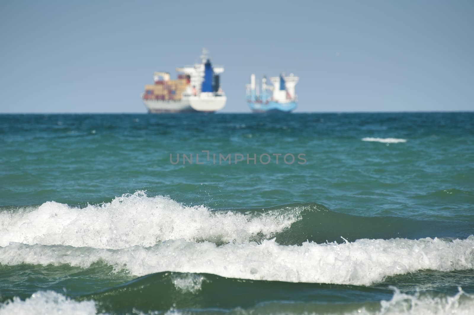 Commercial container ship on blue sky and big waves