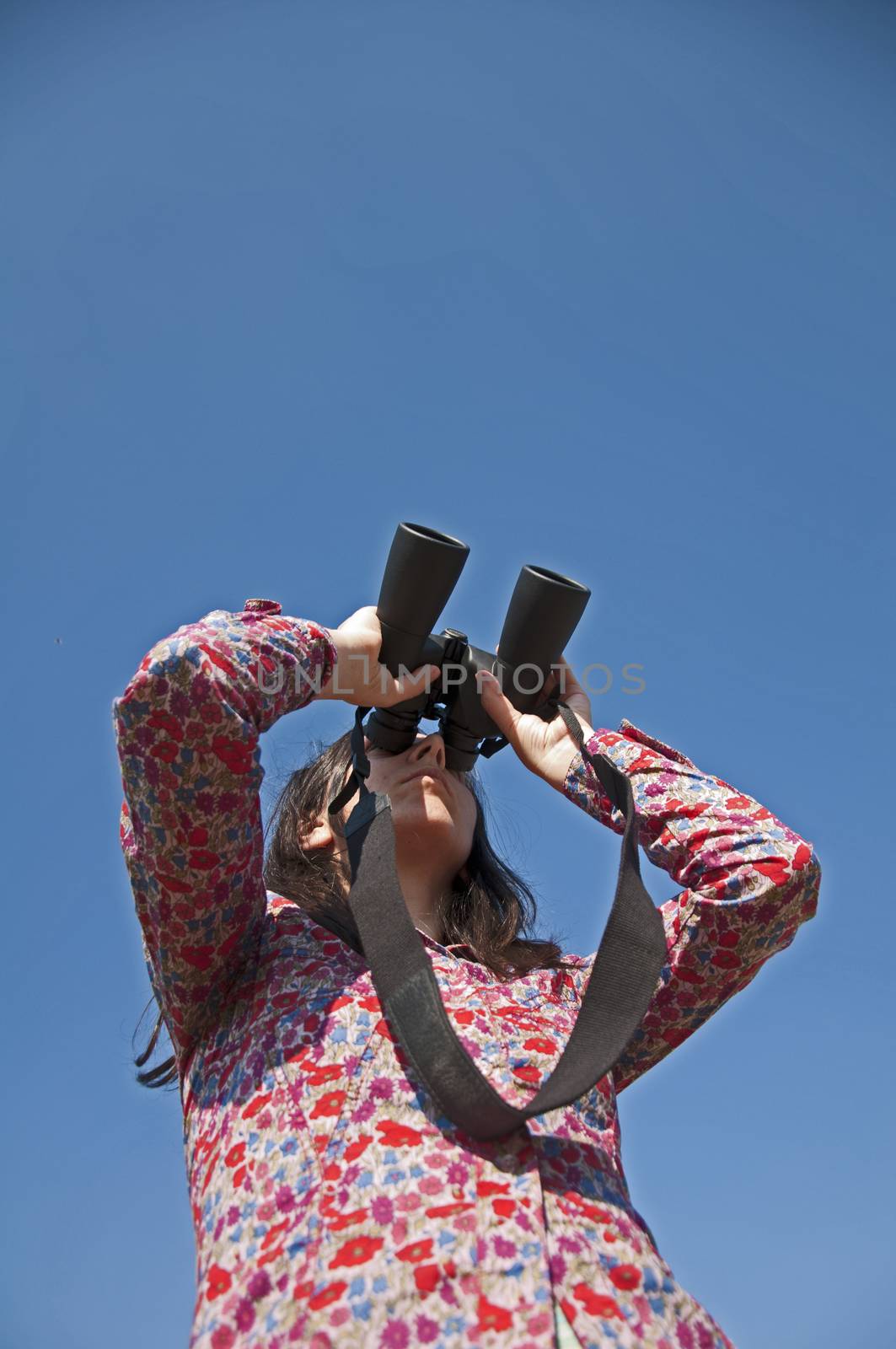 Young woman using binoculars. On blue sky background