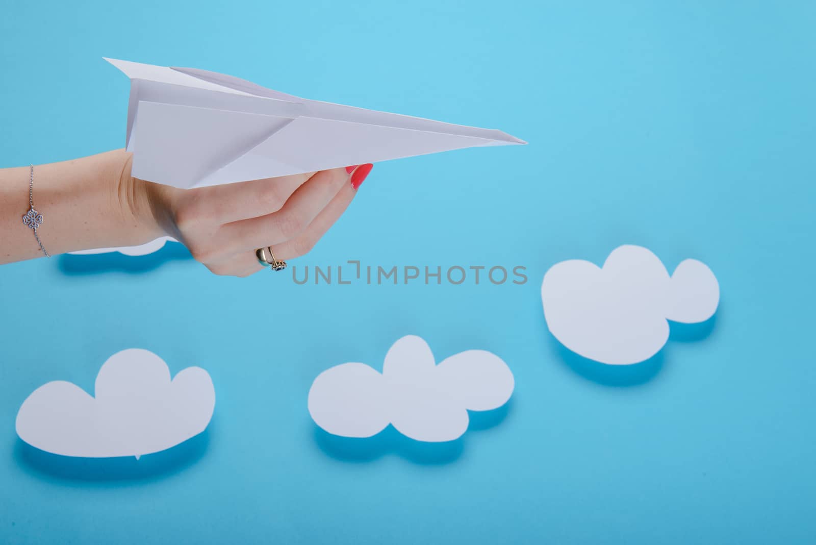 Paper plane in female hand on a blue background with clouds