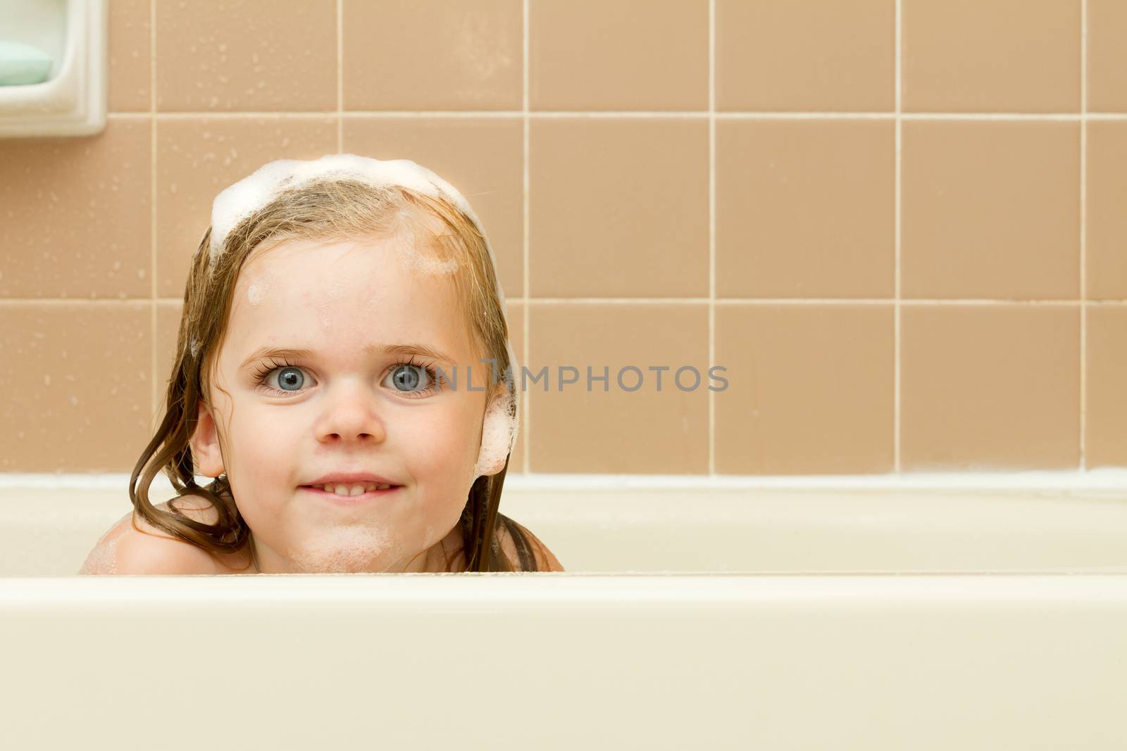 Peeking over the tub while covered in soap, suds, and bubbles.