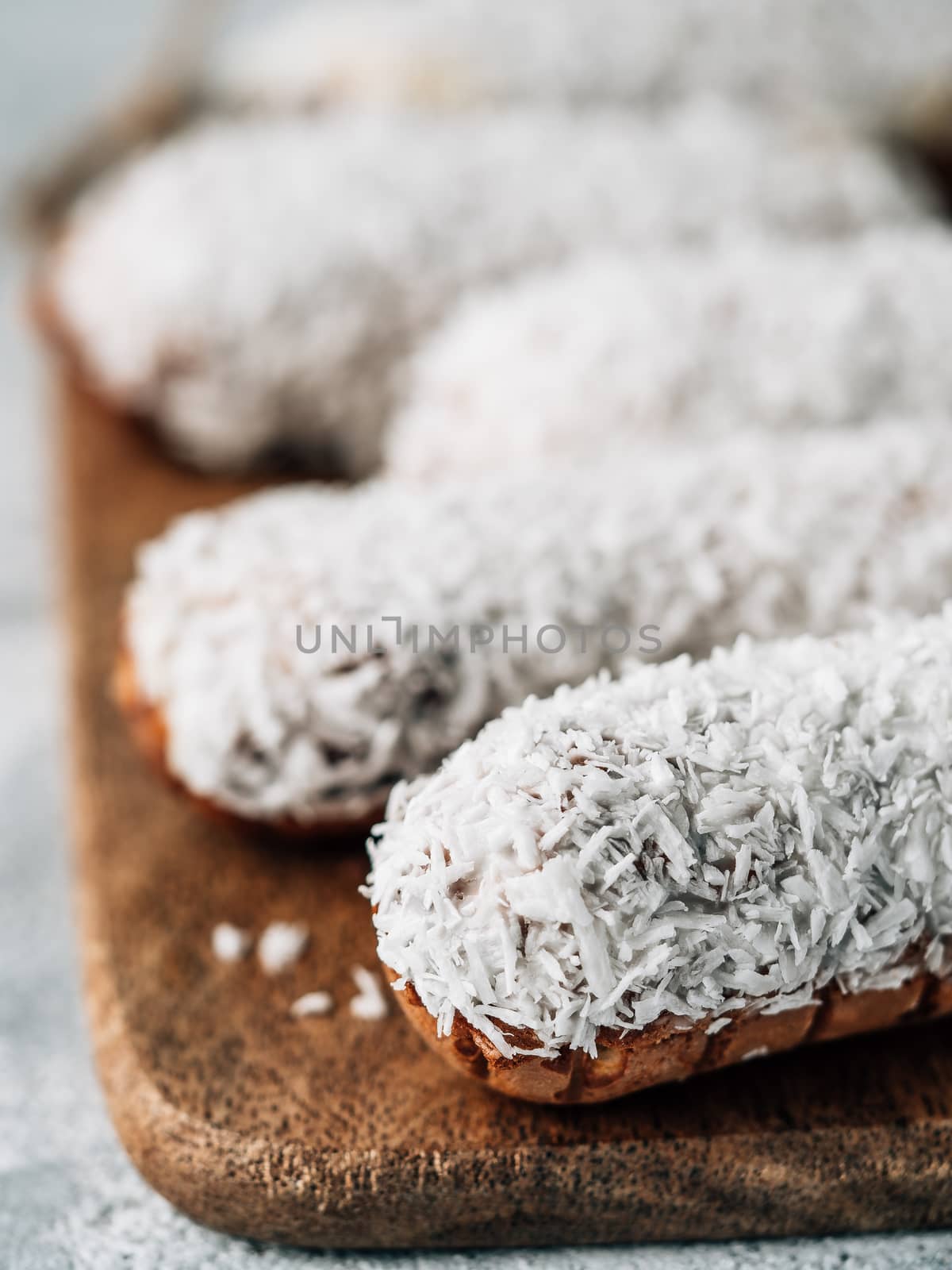 Homemade eclairs with coconut on wooden cutting board. Close up view of delicious healthy profitroles with shredded coconut. Copy space for text or design. Vertical.