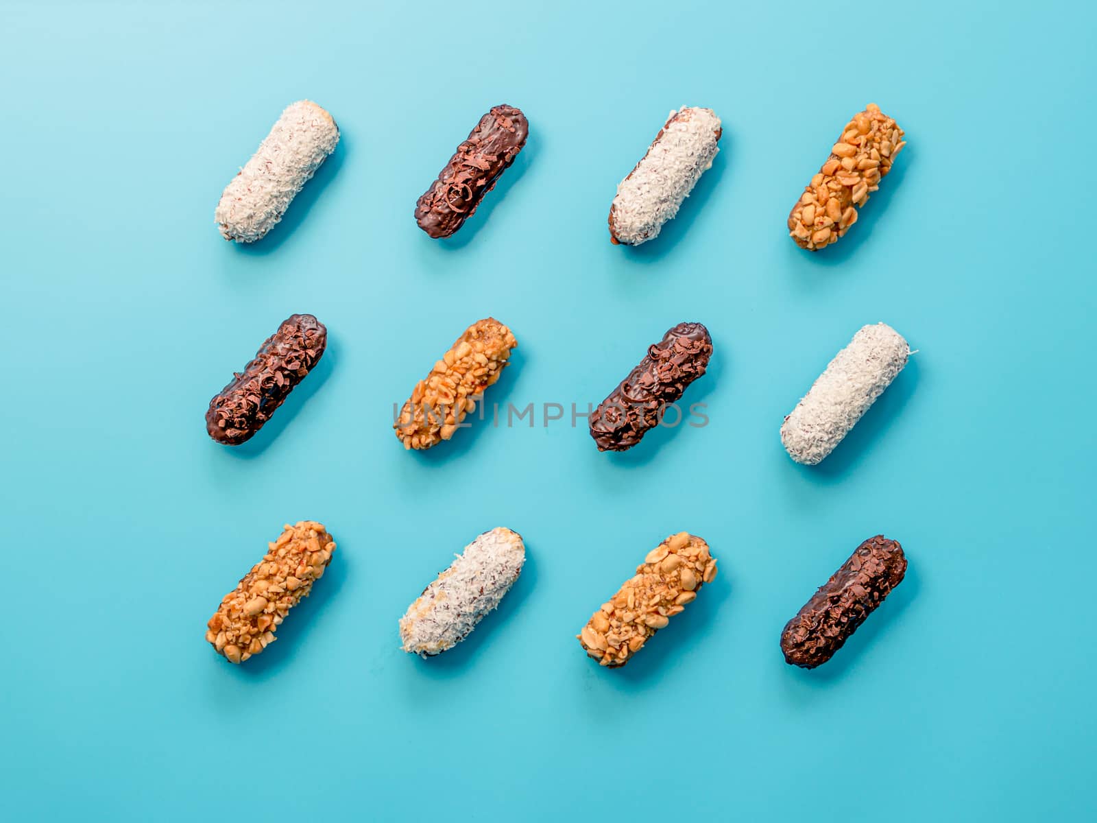 Set of different homemade eclairs on blue background. Top view of delicious healthy profitroles with different decor elements - chocolate, peanut and sherdded coconut