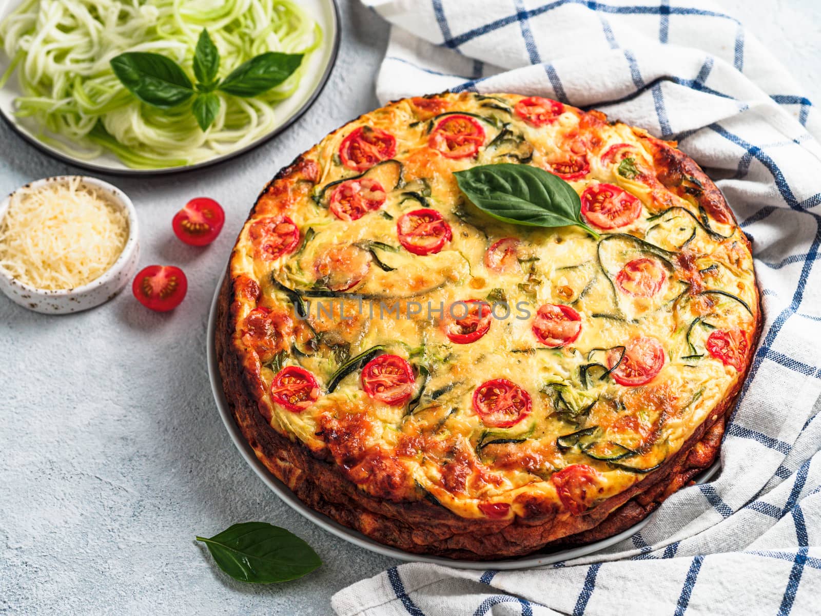 Zucchini pie and ingredients on gray background, copy space left. Delicious savory pie with zucchini, tomatoes, herbs and cheese. Idea and recipe for healthy baking and lot to harvest of zucchini