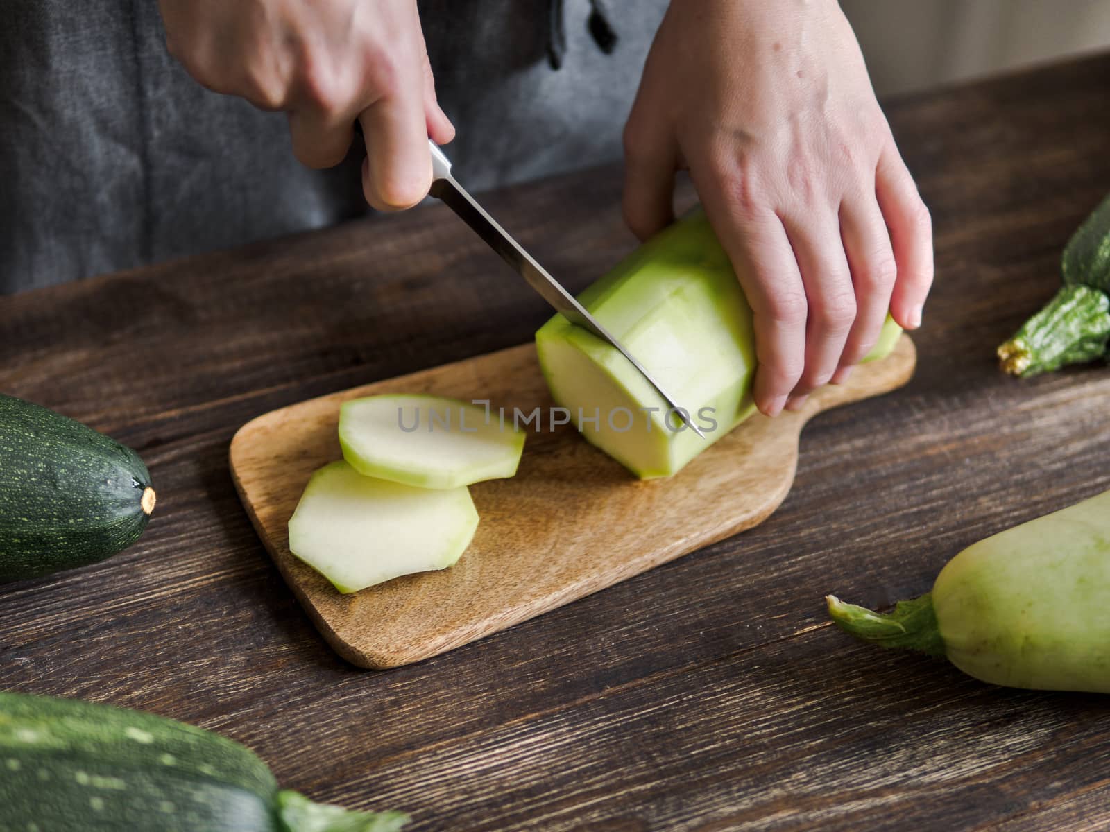 Zucchini harvest. Woman slices zucchini on wooden table. Farm organic zucchini harvesting