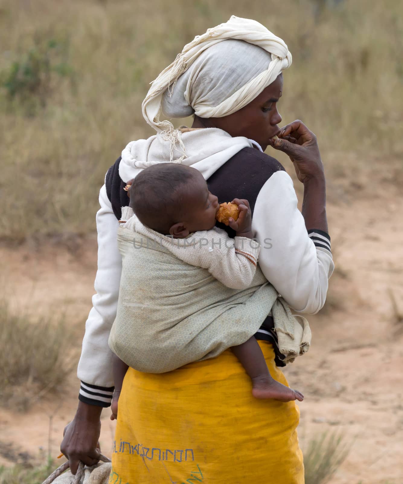 Madagascar on july 29, 2019 - Child eating lunch, hanging on it's mothers back