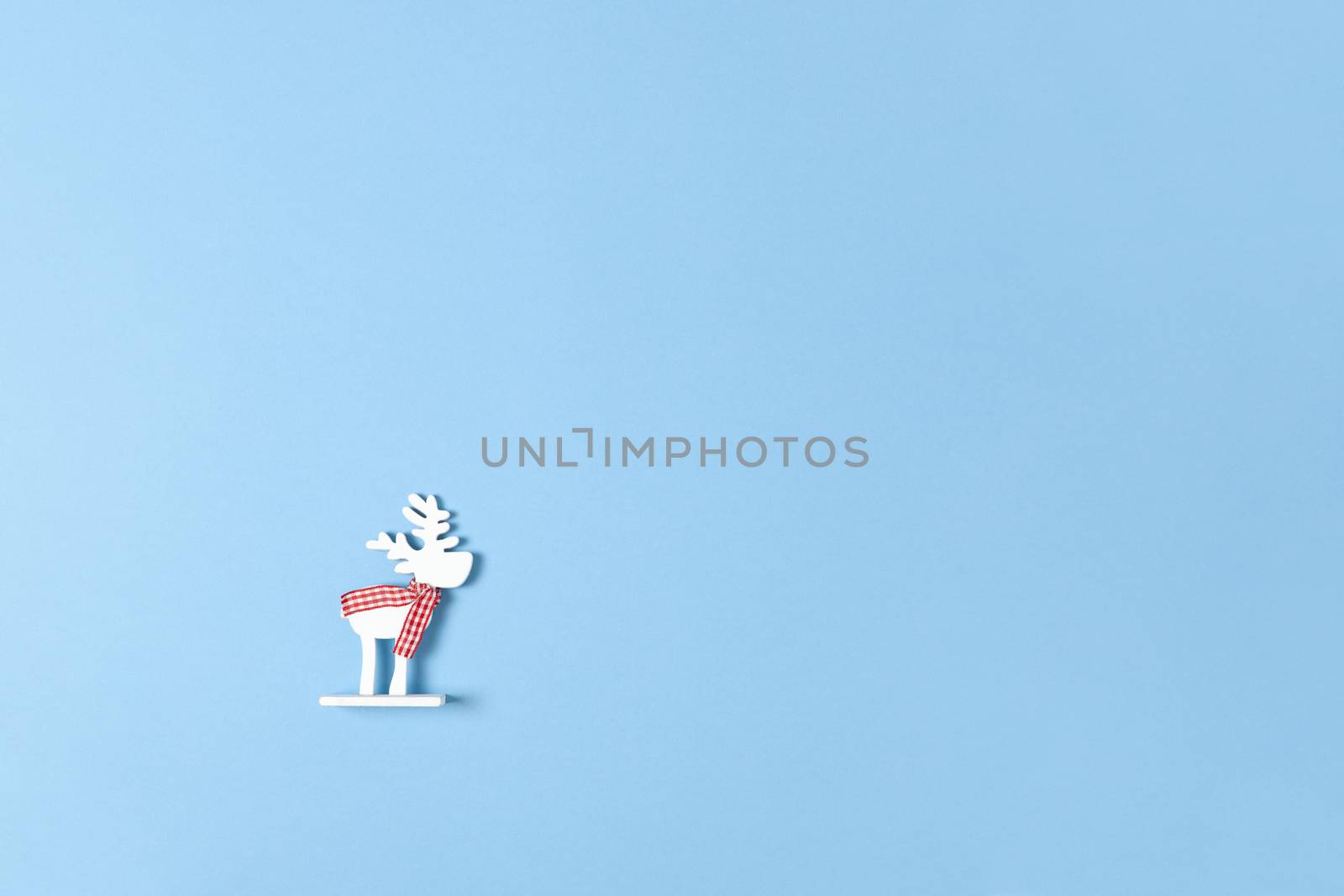 Christmas decoration, toy white deer in checkered scarf on pastel blue background with copy space. Festive, New Year concept. Horizontal, flat lay. Minimal style. Top view.