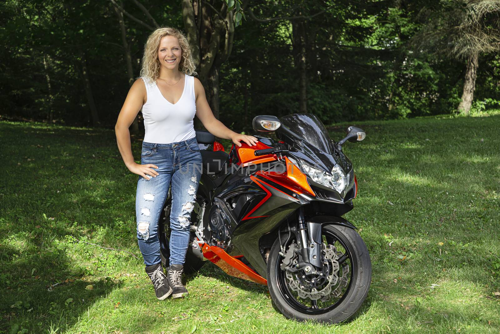 twenty something blond woman, standing beside her sport motocycle, in a park