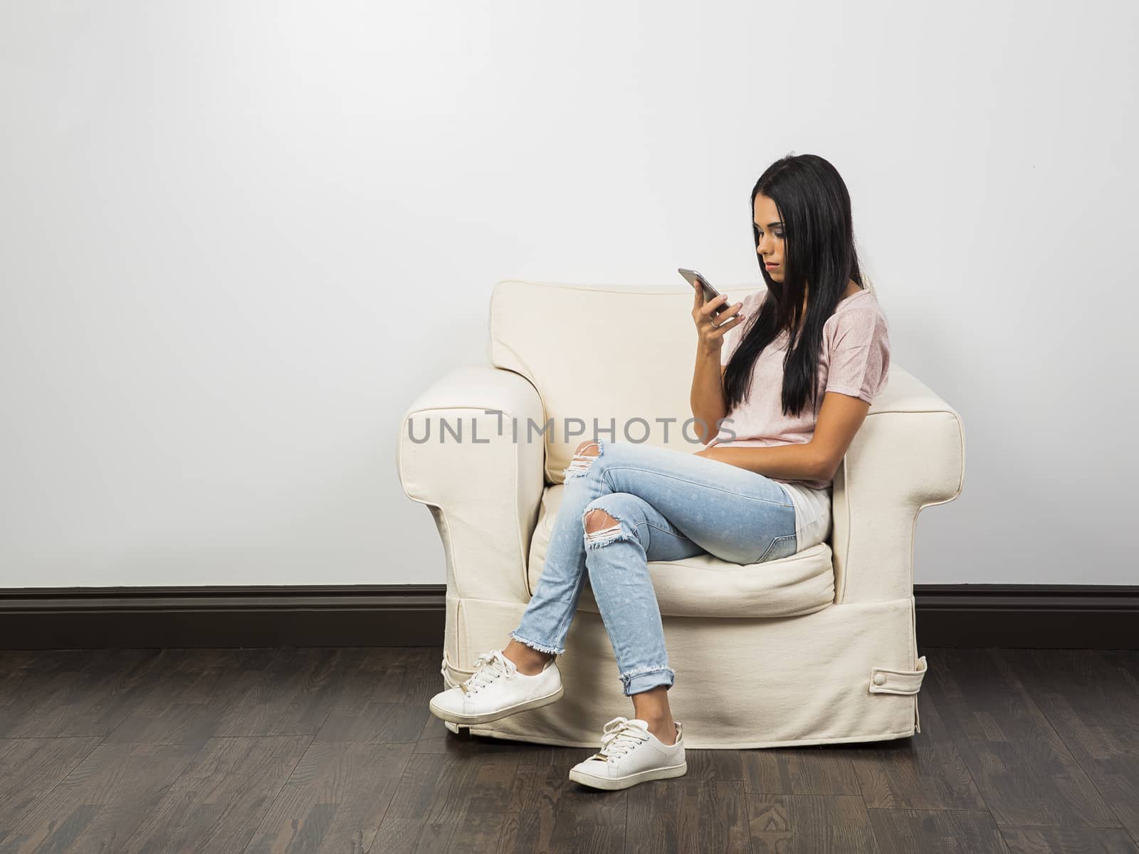young woman sitting on a white couch, looking at her phone
